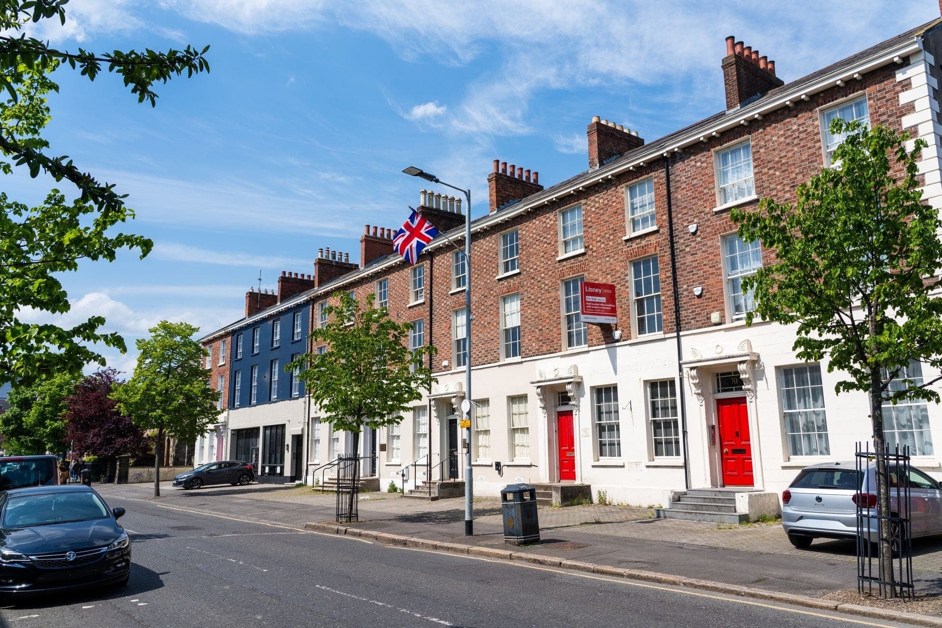 Eine Reihe klassischer georgianischer Reihenhäuser in Dublin mit roten Backsteinfassaden, weißen Türen und hohen Schiebefenstern unter einem strahlend blauen Himmel.