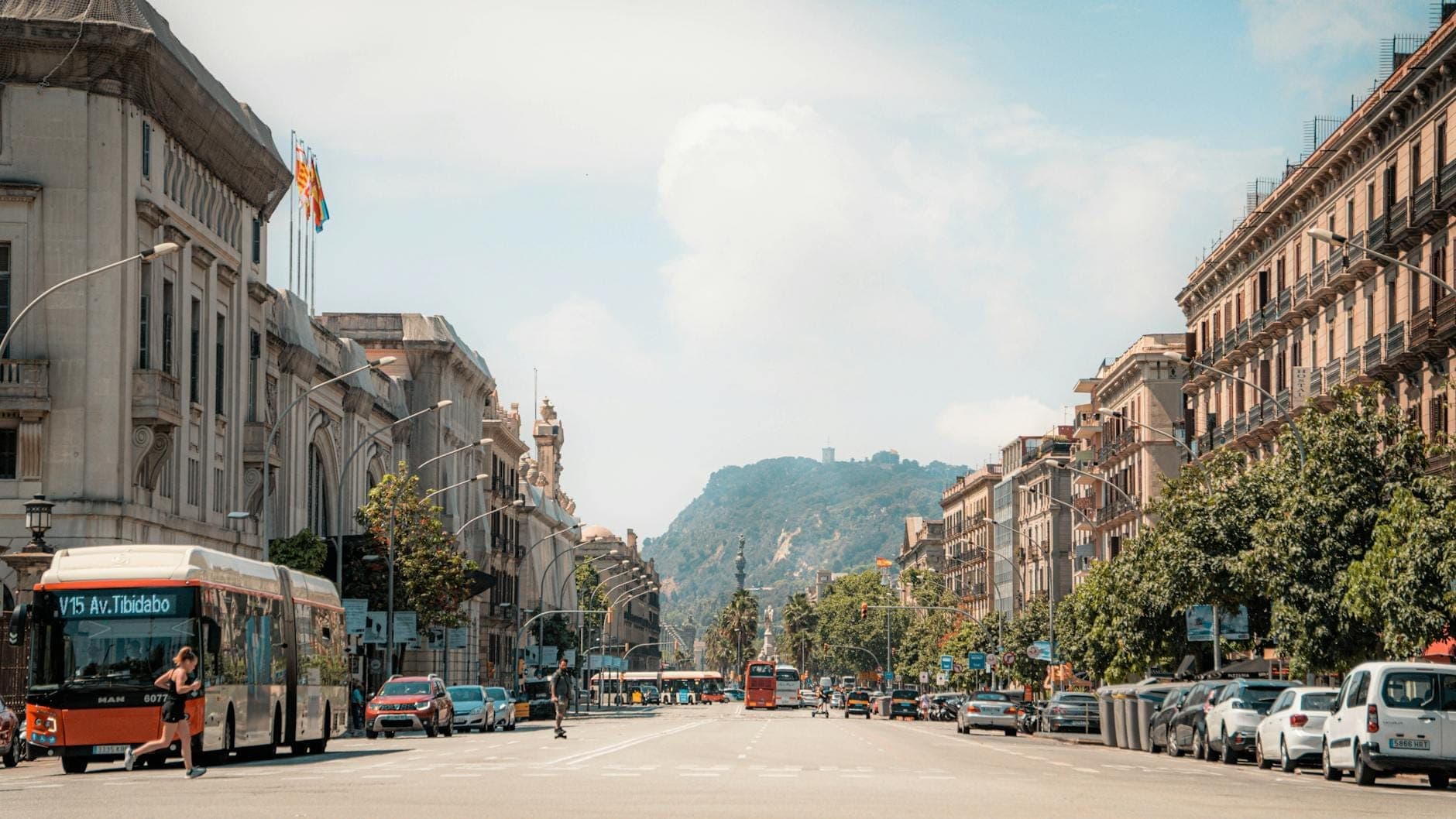 Cảnh phố rộng ở Barcelona với xe buýt, taxi và ô tô, hai bên là những tòa nhà lịch sử và đồi núi xa xa — minh họa các phương tiện giao thông đô thị đa dạng.