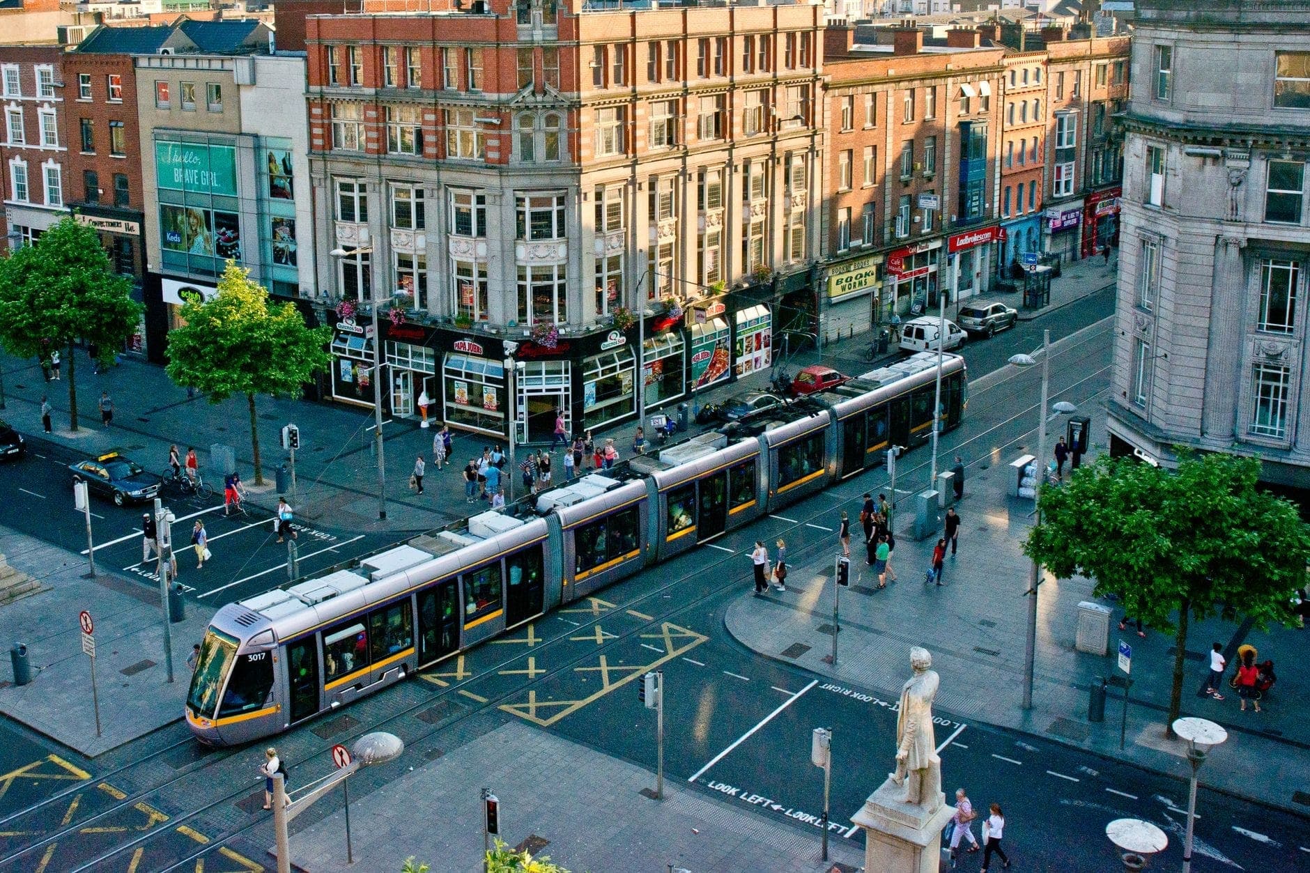Luftaufnahme der Dubliner Innenstadt mit einer modernen Luas-Tram an einer belebten Kreuzung, umgeben von historischen Gebäuden und lebhaften Straßen.