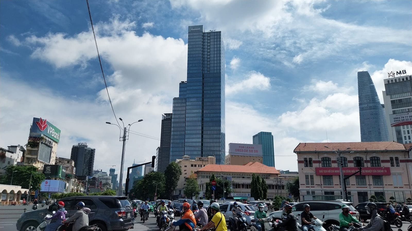 Cảnh đường phố TP.HCM tấp nập xe máy và ô tô, các tòa nhà chọc trời hiện đại và bầu trời xanh, lột tả không khí giao thông sôi động của thành phố.