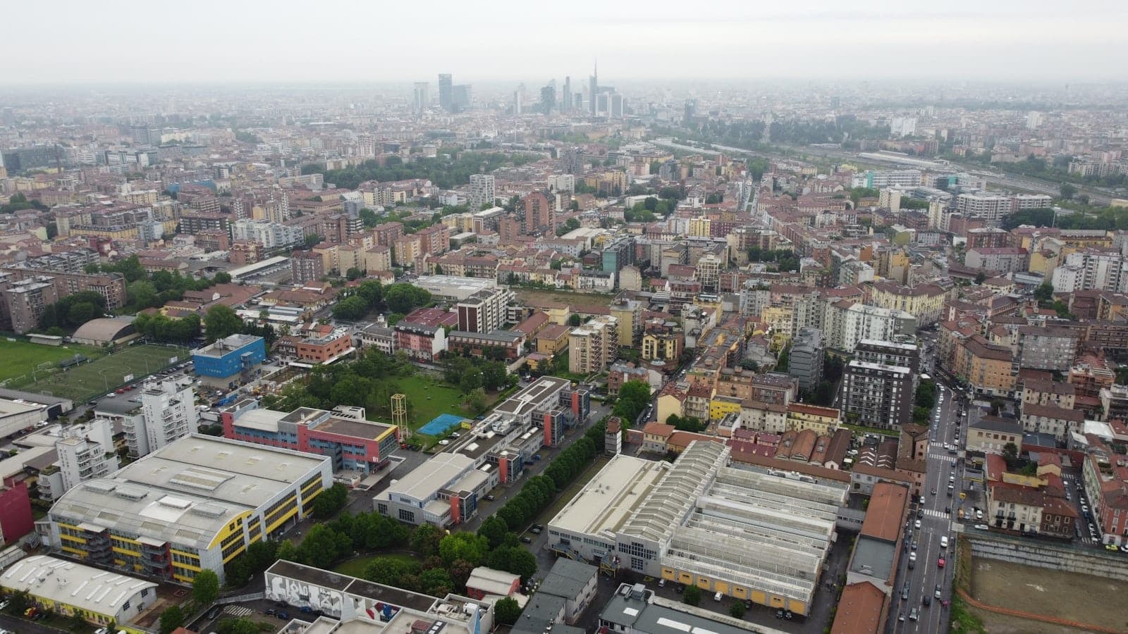 Luftpanoramamblick über Mailand mit Stadtteilen, Straßen und der Skyline in der Ferne sowie einer Mischung aus Gebäuden und Grünflächen.
