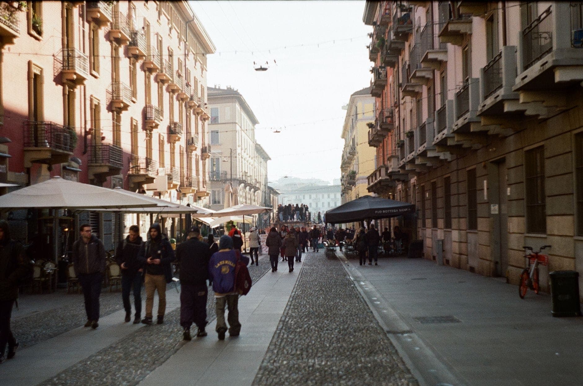Fußgängerzone in Mailand mit Spaziergängern, Straßencafés und typisch italienischen Gebäuden auf beiden Seiten.