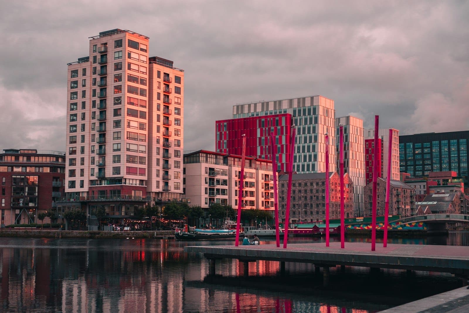 Le Grand Canal Dock avec ses poteaux rouges caractéristiques, ses immeubles en verre contemporains et leurs reflets dans l'eau au coucher de soleil, sous un ciel dramatique à Dublin.