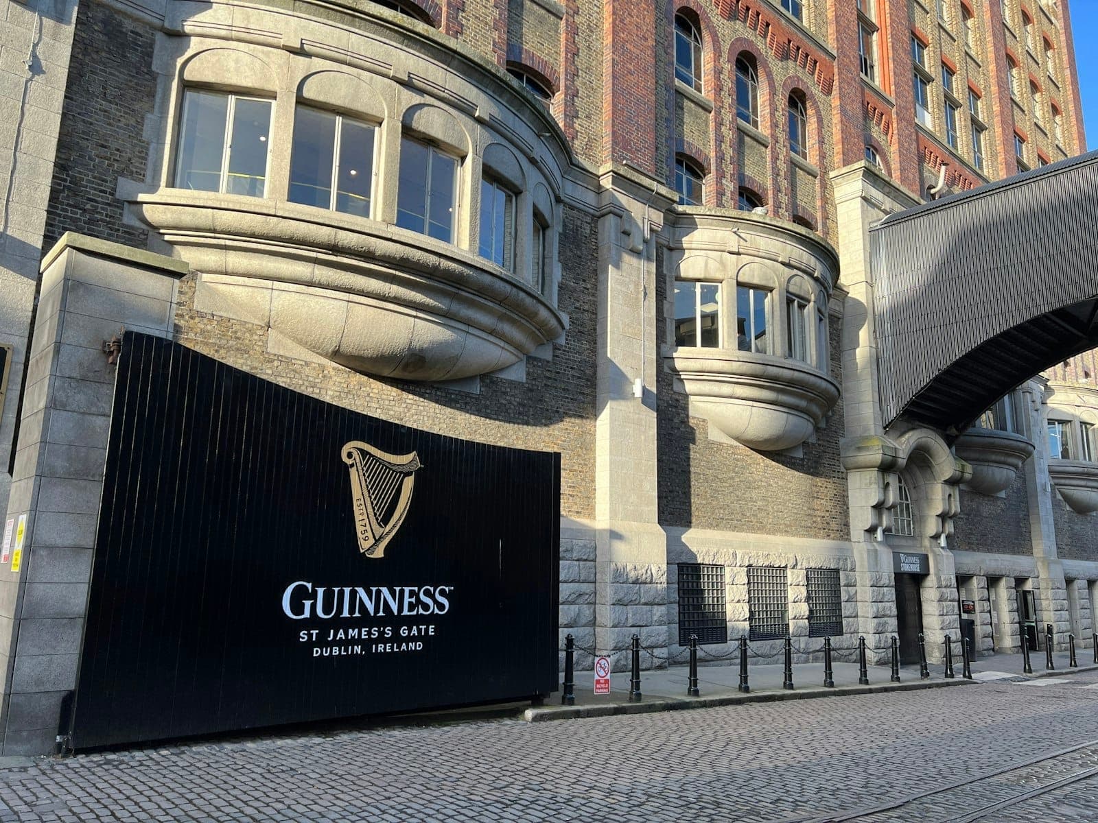 ภาพภายนอกของ Guinness Storehouse ที่ St James's Gate ในดับลิน เห็นซุ้มประตูไอคอนิก ผนังอิฐทรงคลาสสิก และถนนพื้นหิน