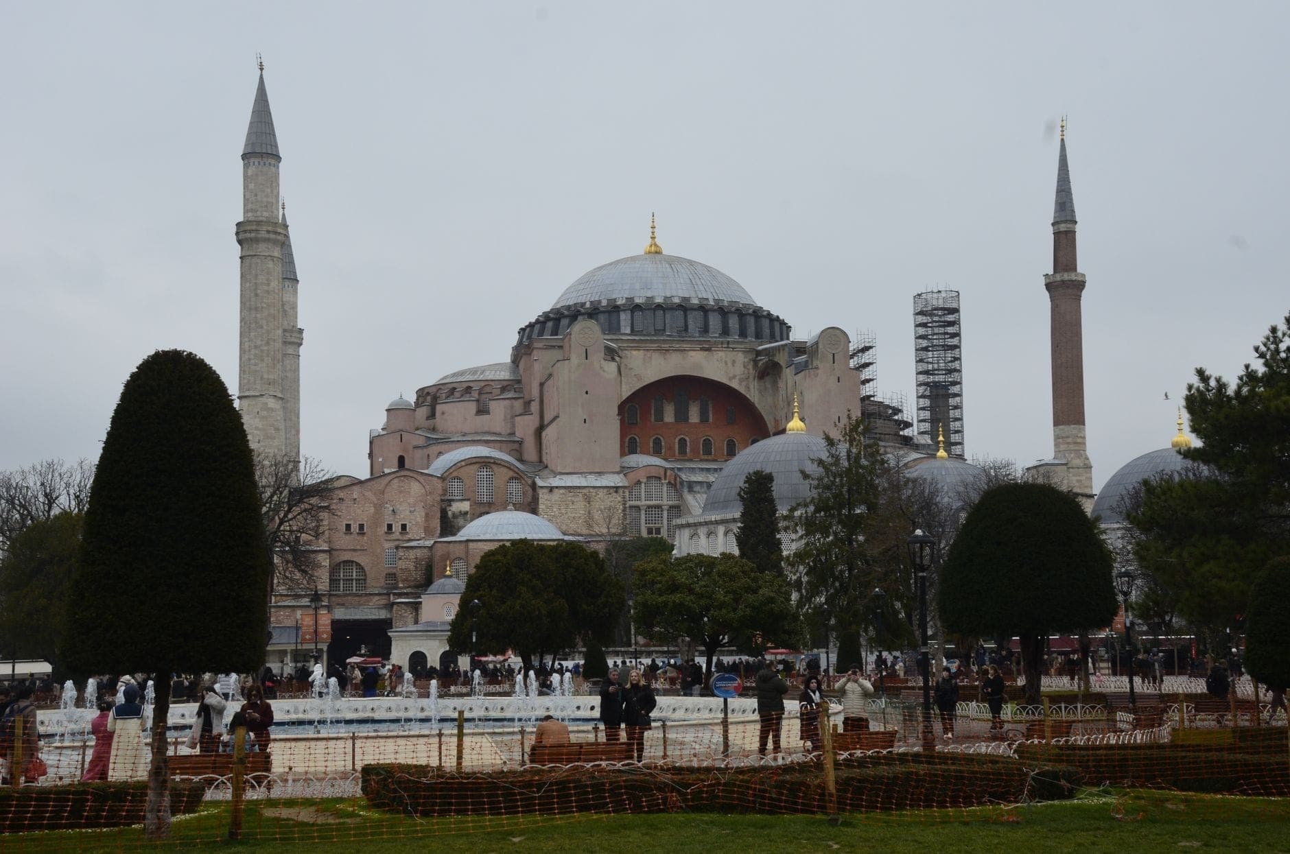 Weitwinkelansicht der Hagia Sophia mit Kuppeln und Minaretten, umgeben von Bäumen, Gärten und Besuchern unter einem bedeckten Himmel.
