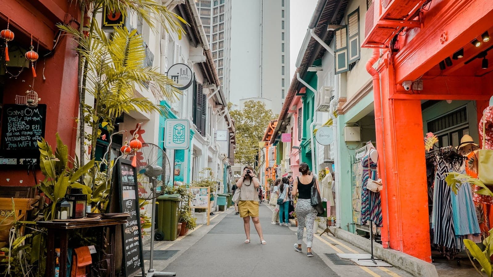 Colorful narrow street of Haji Lane with pastel shophouses, vibrant storefronts, outdoor plants, and people exploring the lively lane in daylight.