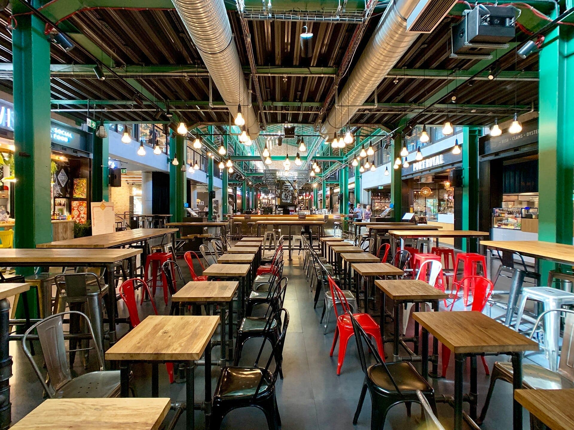 Reihen von Holztischen und bunten Metallstühlen im geräumigen Interieur im Industriestil der Hala Koszyki Food Hall in Warschau.