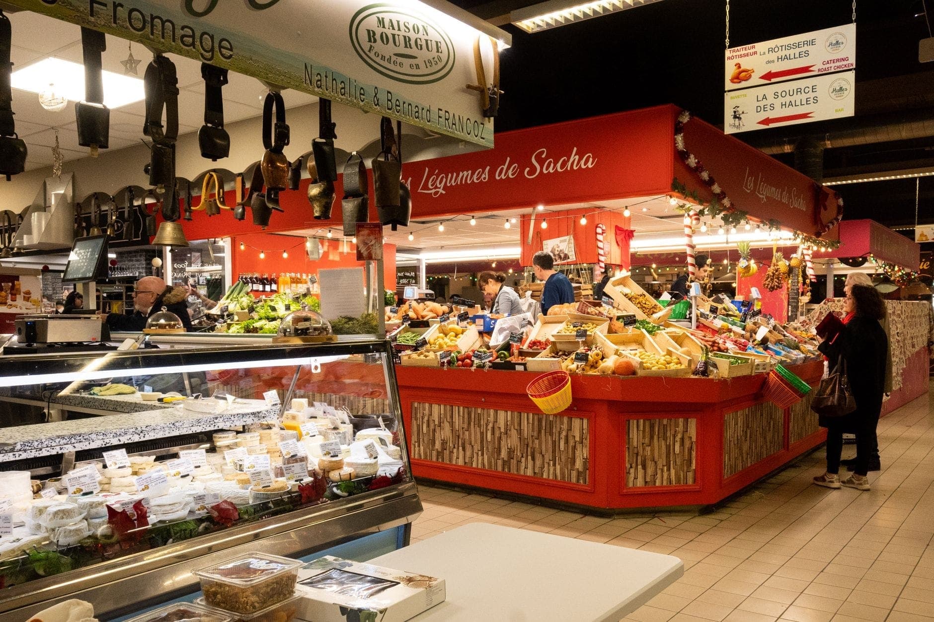 Bên trong chợ Halles Centrales ở Le Havre, các gian hàng nông sản đầy màu sắc và quầy phô mai được trưng bày dưới ánh đèn trong nhà sáng rực với những người mua sắm đang dạo quanh.