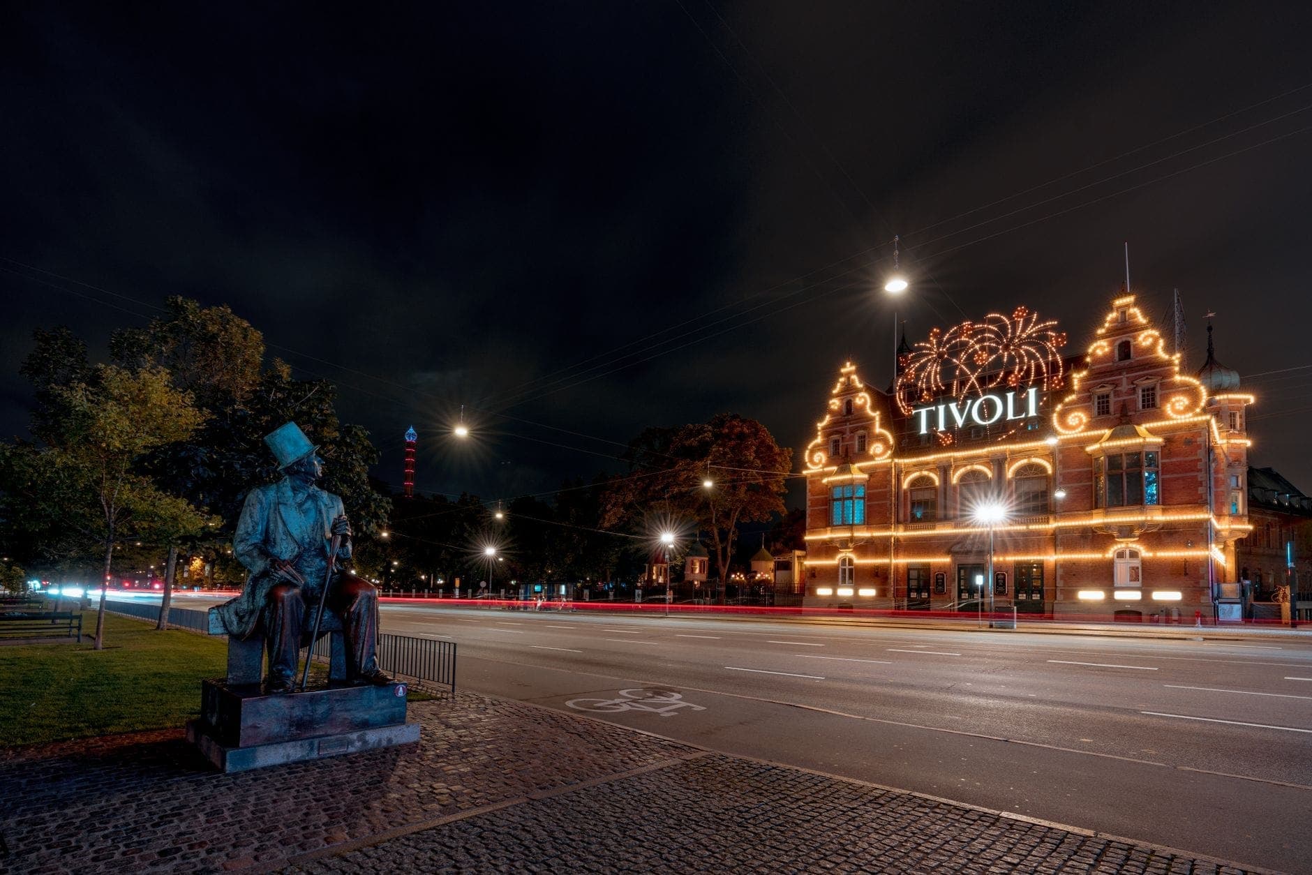 Nächtliche Szene am Eingang des Tivoli in Kopenhagen, festlich beleuchtet, mit einer Bronzestatue von Hans Christian Andersen im Vordergrund, der nachdenklich auf die Stadt blickt.