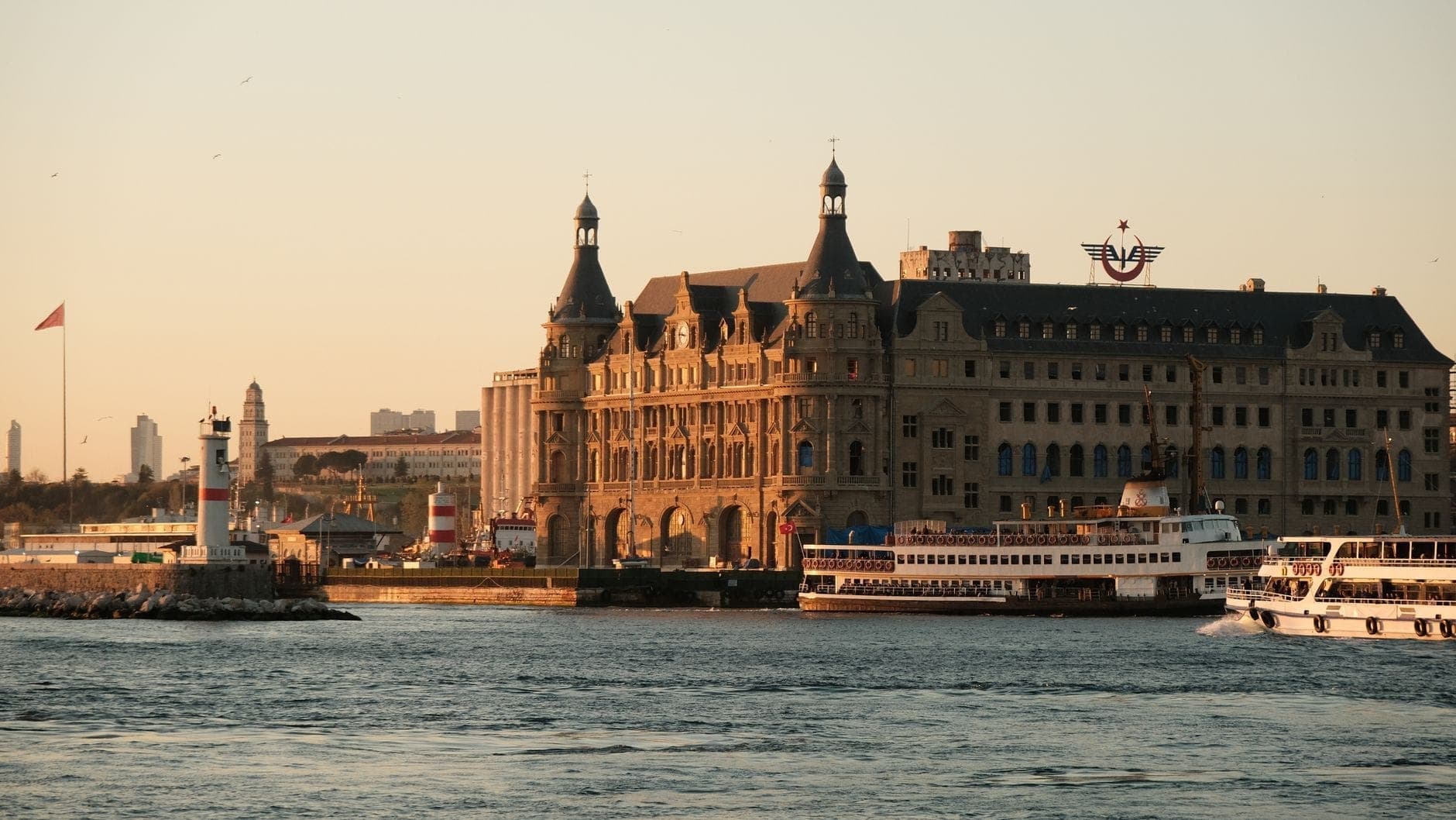 Bahnhof Haydarpaşa zur goldenen Stunde: warmes Sonnenlicht auf der neobarocken Fassade, Fähren im Vordergrund und das Wasser des Bosporus, das das historische Gebäude widerspiegelt.