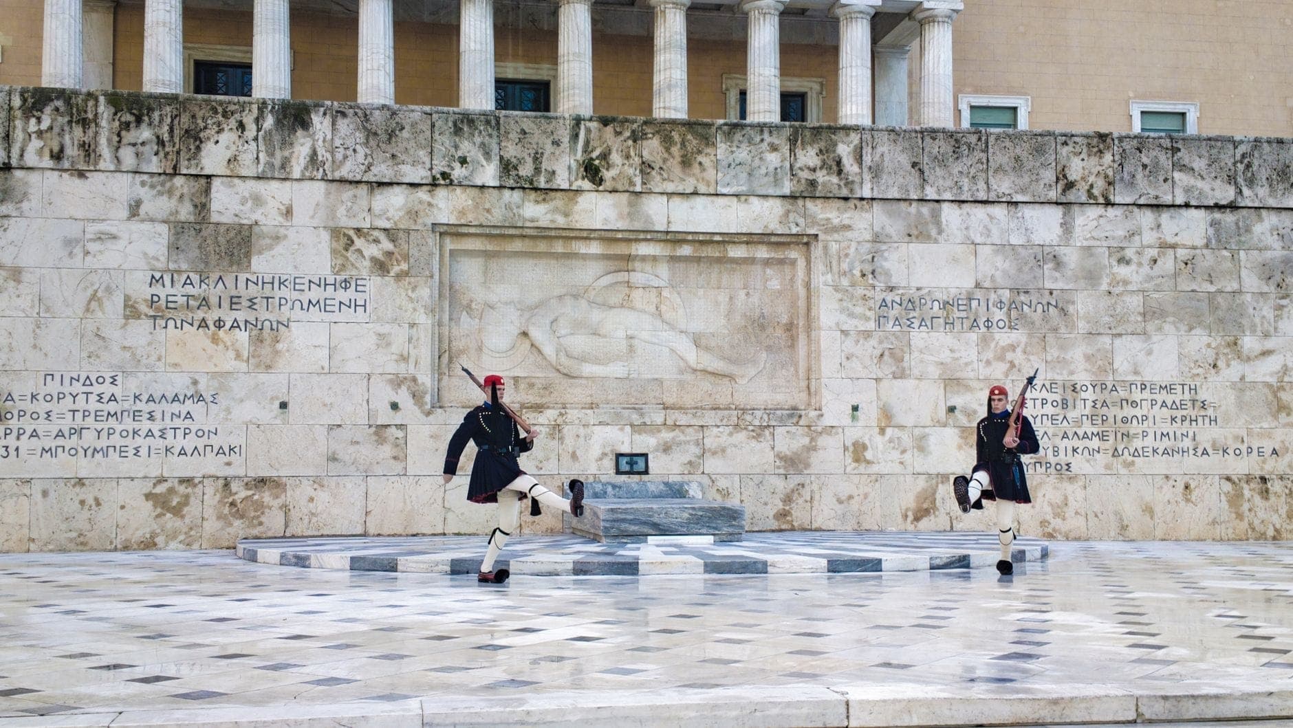 Two Evzones guards in ceremonial uniform perform the changing of the guard in front of the Tomb of the Unknown Soldier and Hellenic Parliament in Athens.