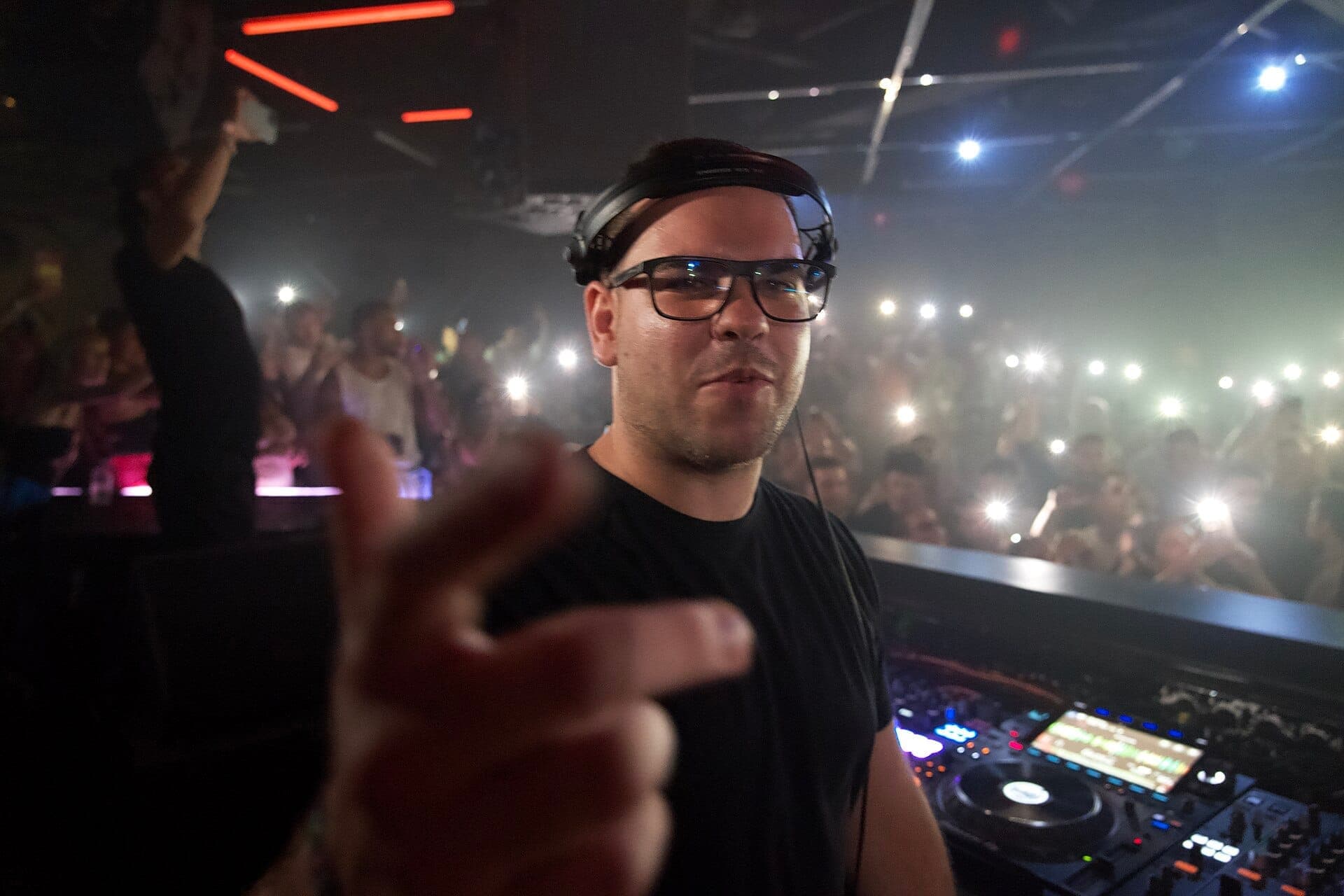 A DJ performs in front of a lively crowd at Hï Ibiza, with flashing lights and electronic music equipment visible on a dark, crowded dance floor.