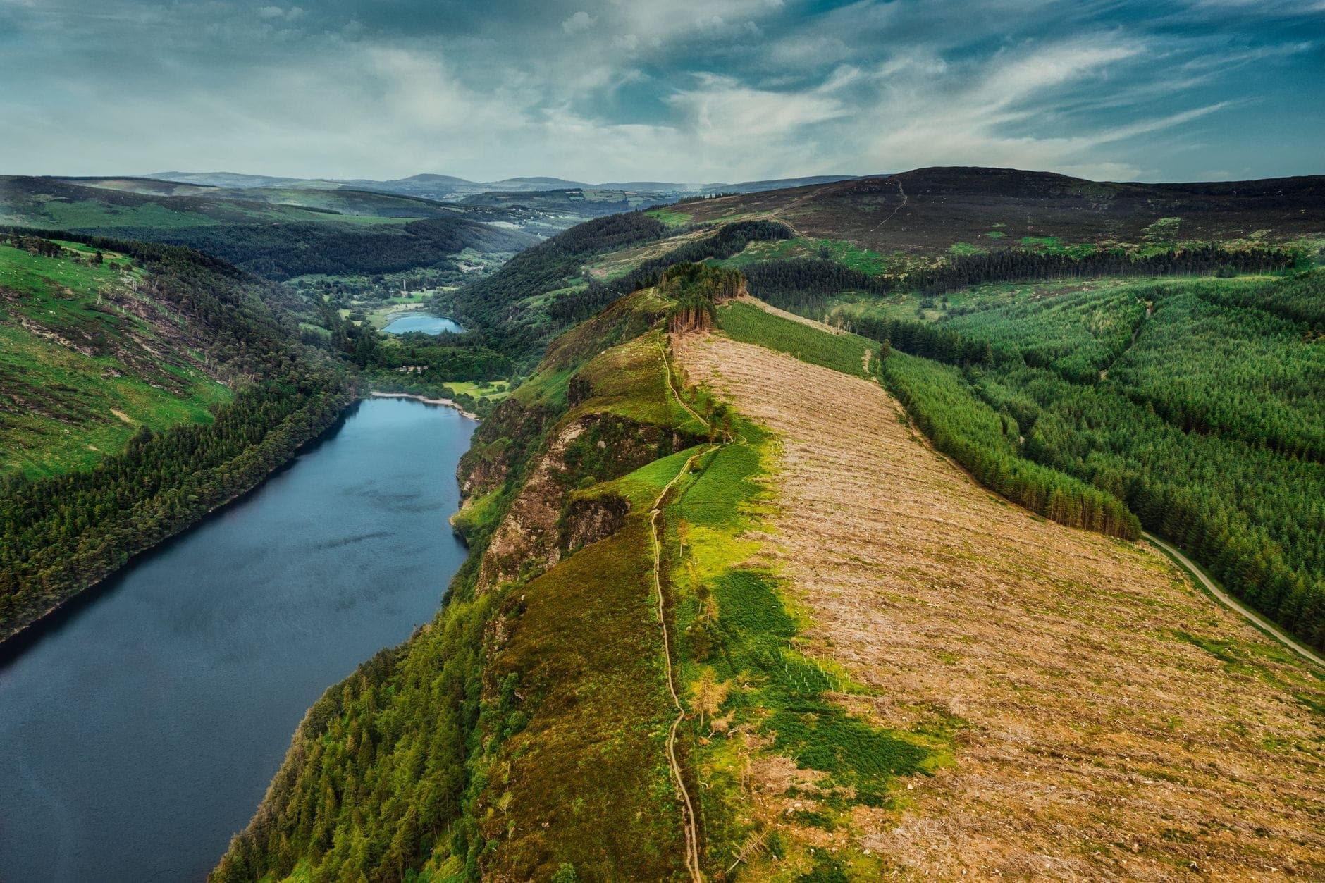 Vista aerea di una valle glaciale e di un lago circondati da foreste verdi e colline nelle Wicklow Mountains in una giornata serena.