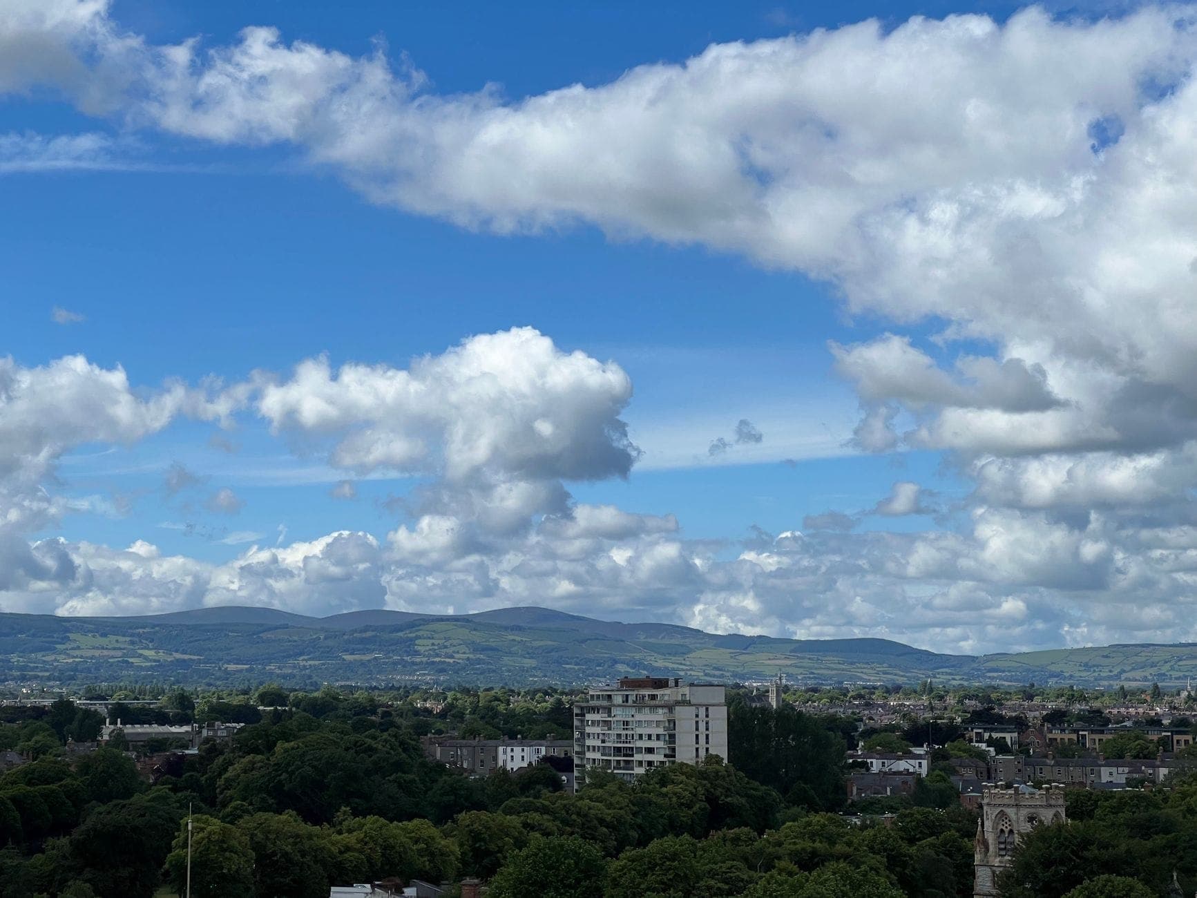 Vista panoramica della città di Dublino con le Dublin Mountains sullo sfondo sotto un cielo parzialmente nuvoloso.