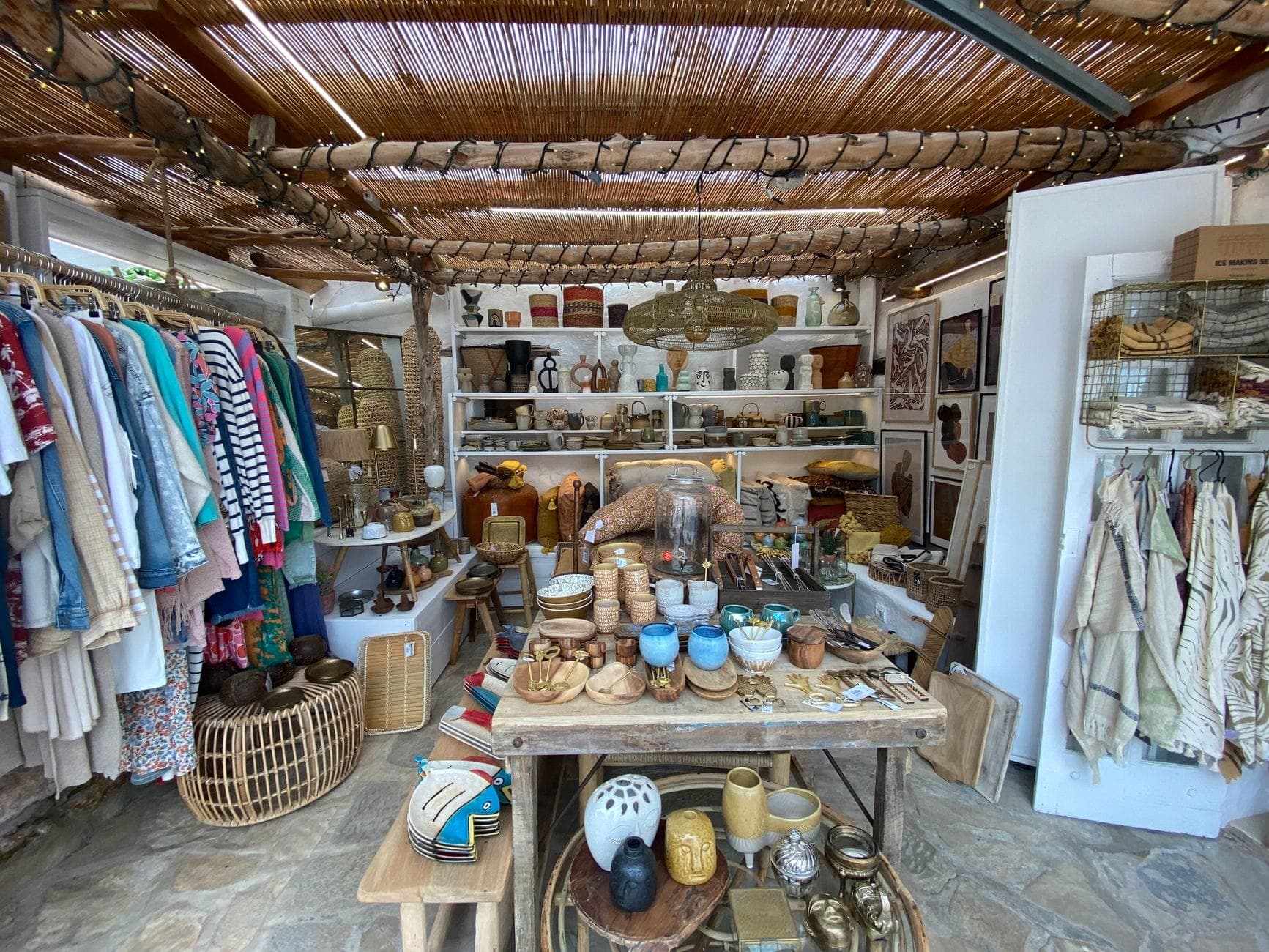 A vibrant open-air market stall with handmade ceramics, jewelry, clothing, and crafts displayed under a rustic canopy, evoking Ibiza’s bohemian hippy spirit.