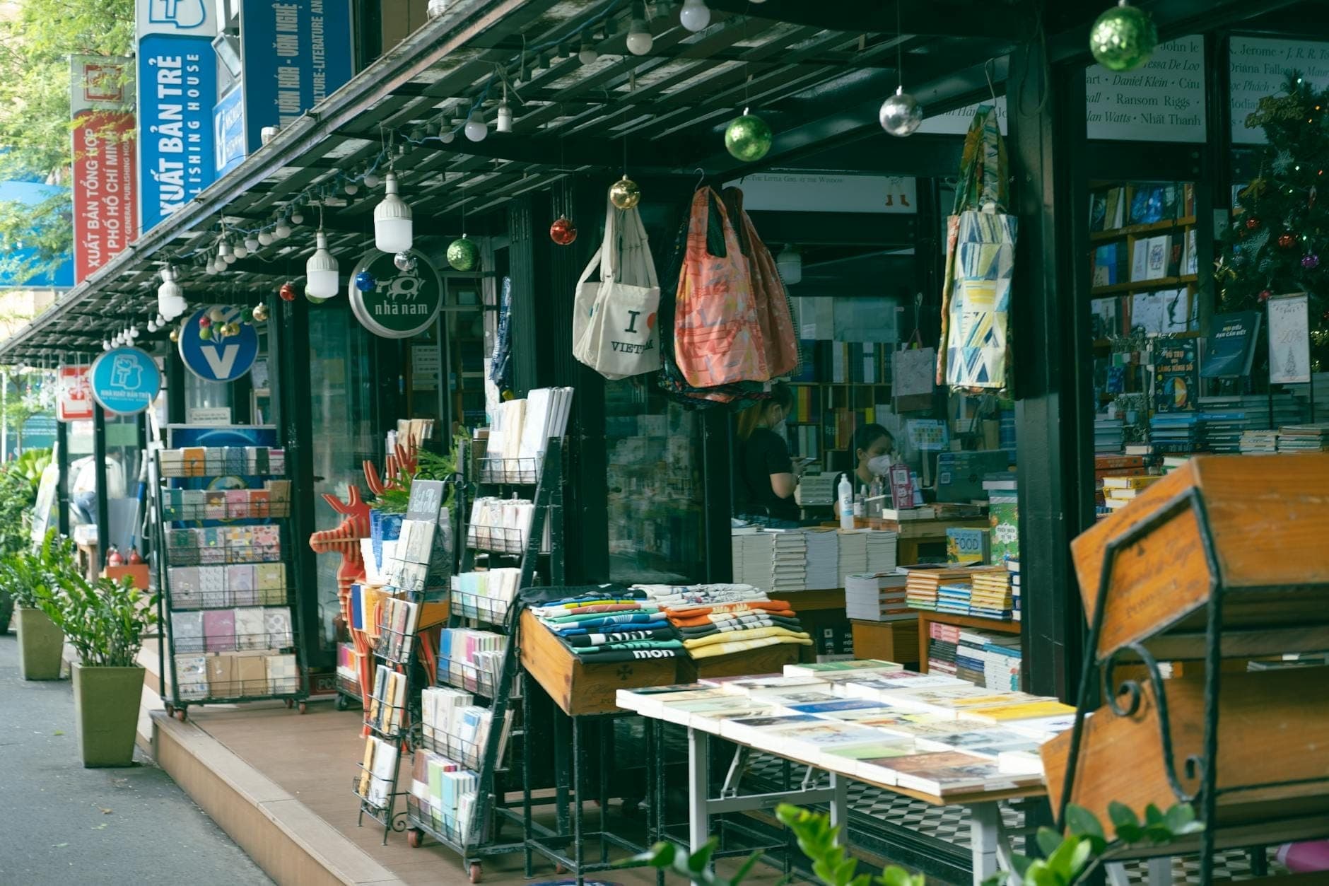Hàng gian sách dưới mái hiên, trưng bày đầy sách và trang trí bằng cây treo cùng túi vải đầy màu sắc trên Đường sách Thành phố Hồ Chí Minh.