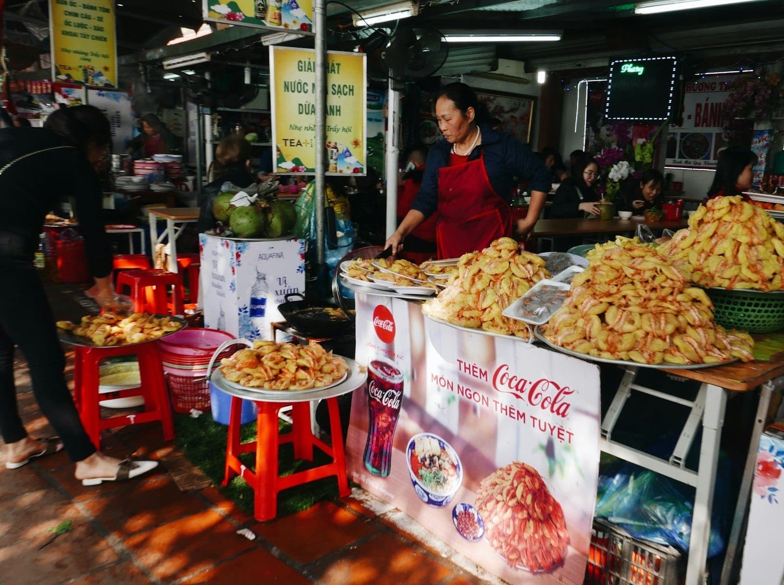 Người phụ nữ bán hàng rong ở Thành phố Hồ Chí Minh đứng sau những mâm bánh xèo thơm phức, xung quanh là biển hiệu đủ màu sắc và những chiếc ghế nhựa nhỏ.