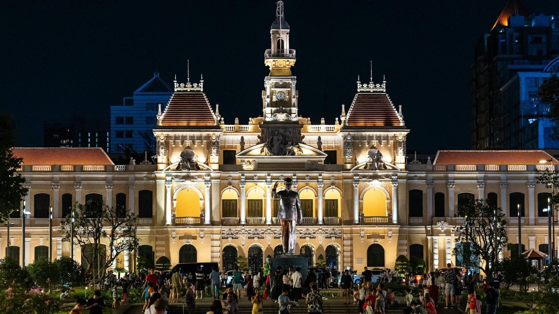 Tượng Hồ Chí Minh về đêm trước tòa nhà Ủy ban Nhân dân Thành phố được chiếu sáng rực rỡ trên phố đi bộ Nguyễn Huệ, với đông đảo người dân tận hưởng bầu không khí sôi động.