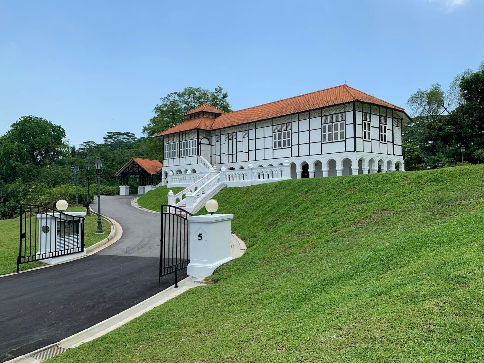 Historic colonial building with white walls and red roof on a grassy hill in Dempsey Hill, Singapore under clear blue sky.