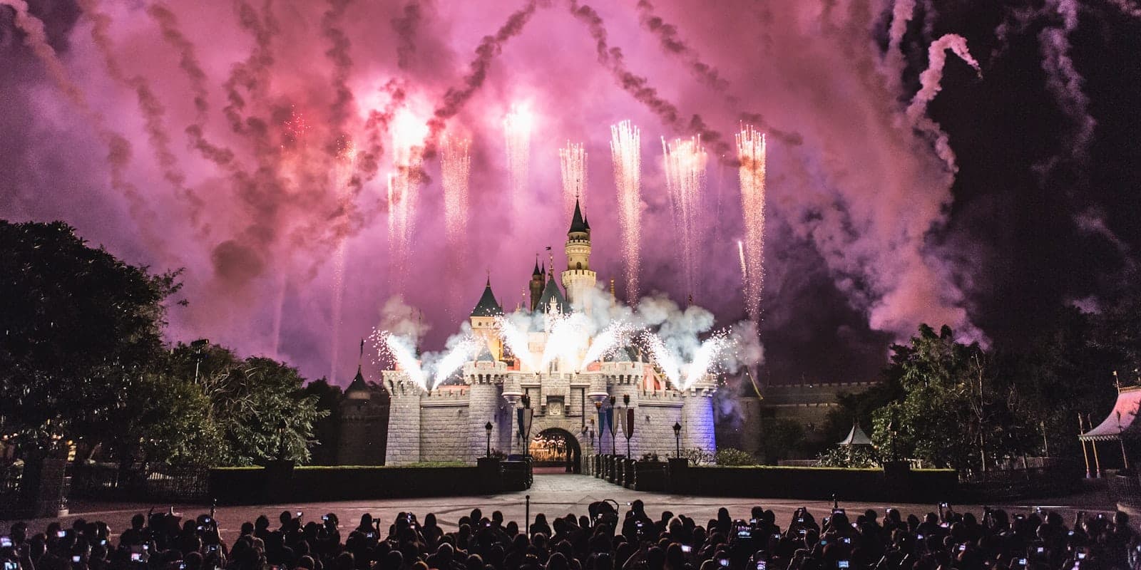 Khung cảnh hoàng hôn mê hoặc tại Hong Kong Disneyland, với lâu đài được chiếu sáng rực rỡ giữa ánh đèn lễ hội và sự hào hứng.