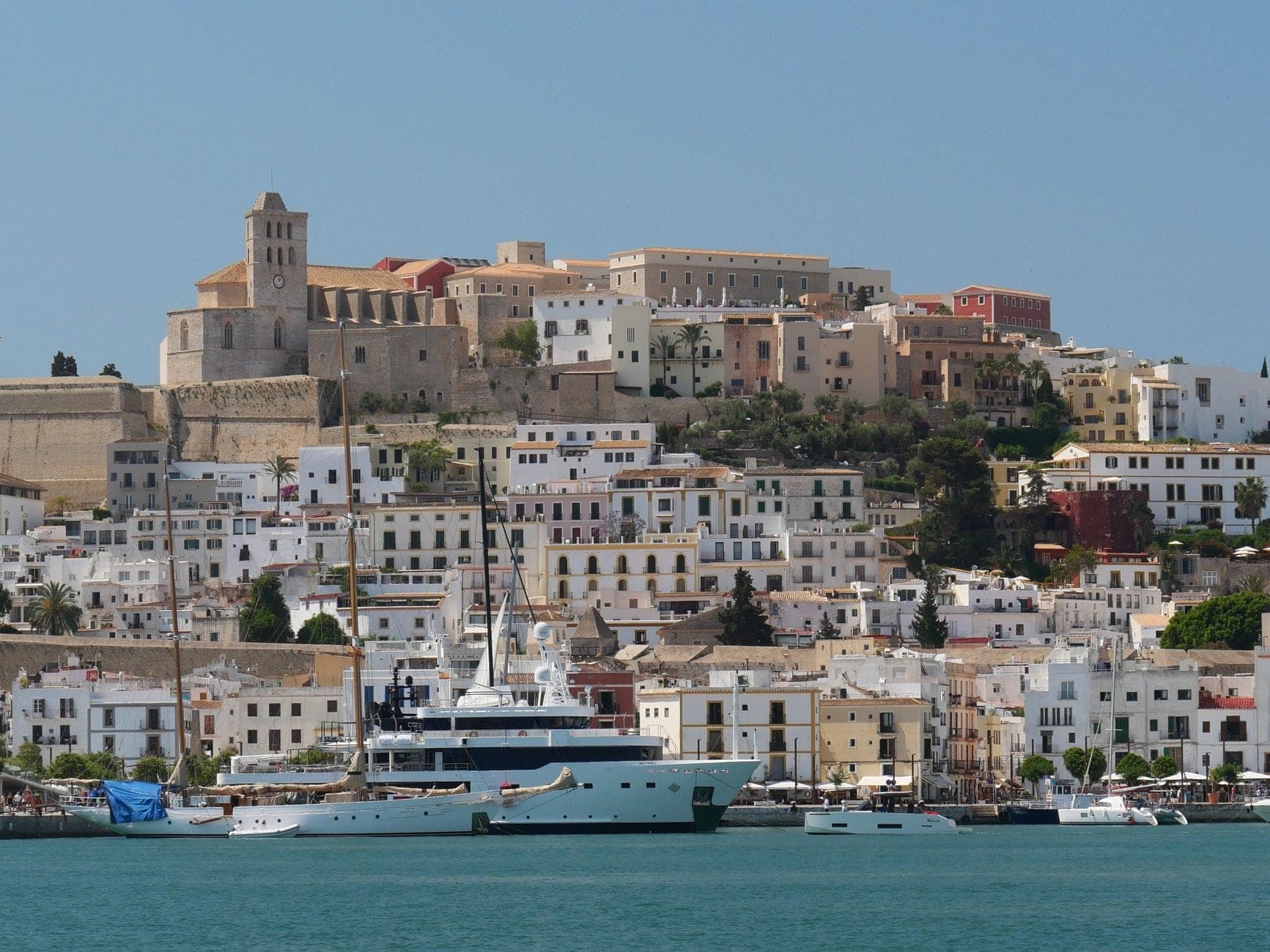 View of Ibiza's old town and Renaissance walls rising above the harbor, with white buildings and yachts in the foreground.