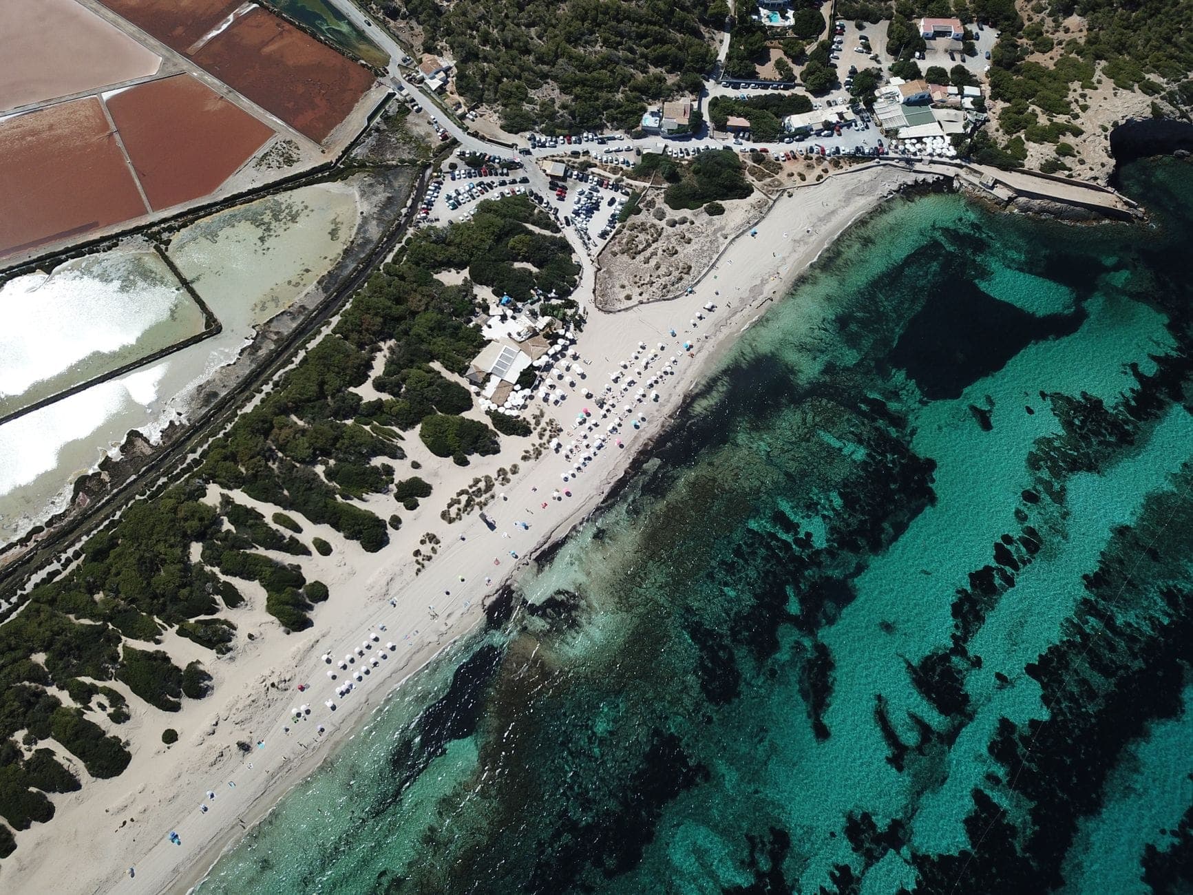 Aerial view of Ses Salines beach with turquoise water, white sand, salt flats, and natural park landscape in southern Ibiza.
