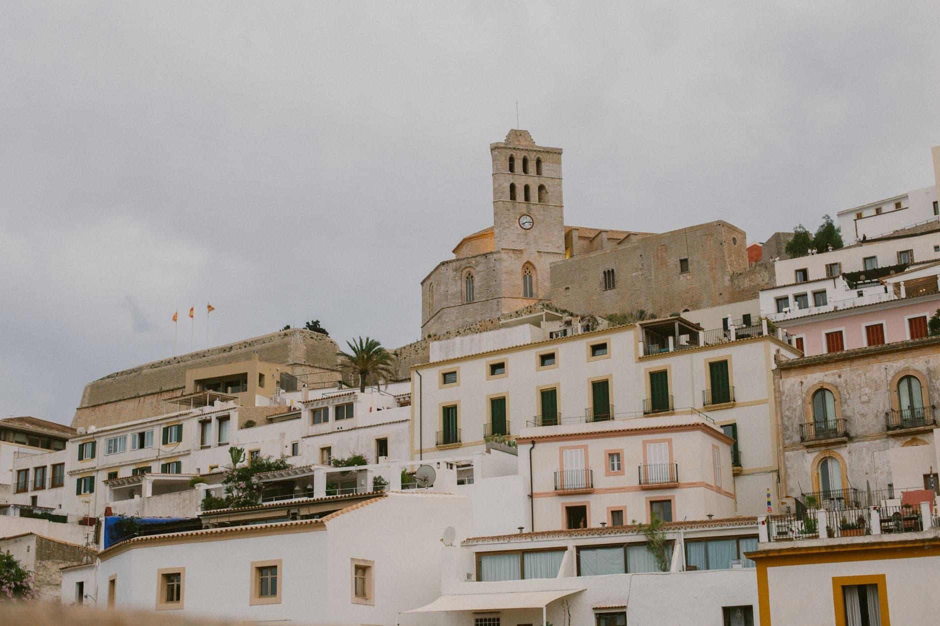 View of Dalt Vila's old town in Ibiza, featuring stone buildings, a clock tower, and whitewashed houses on a hillside.
