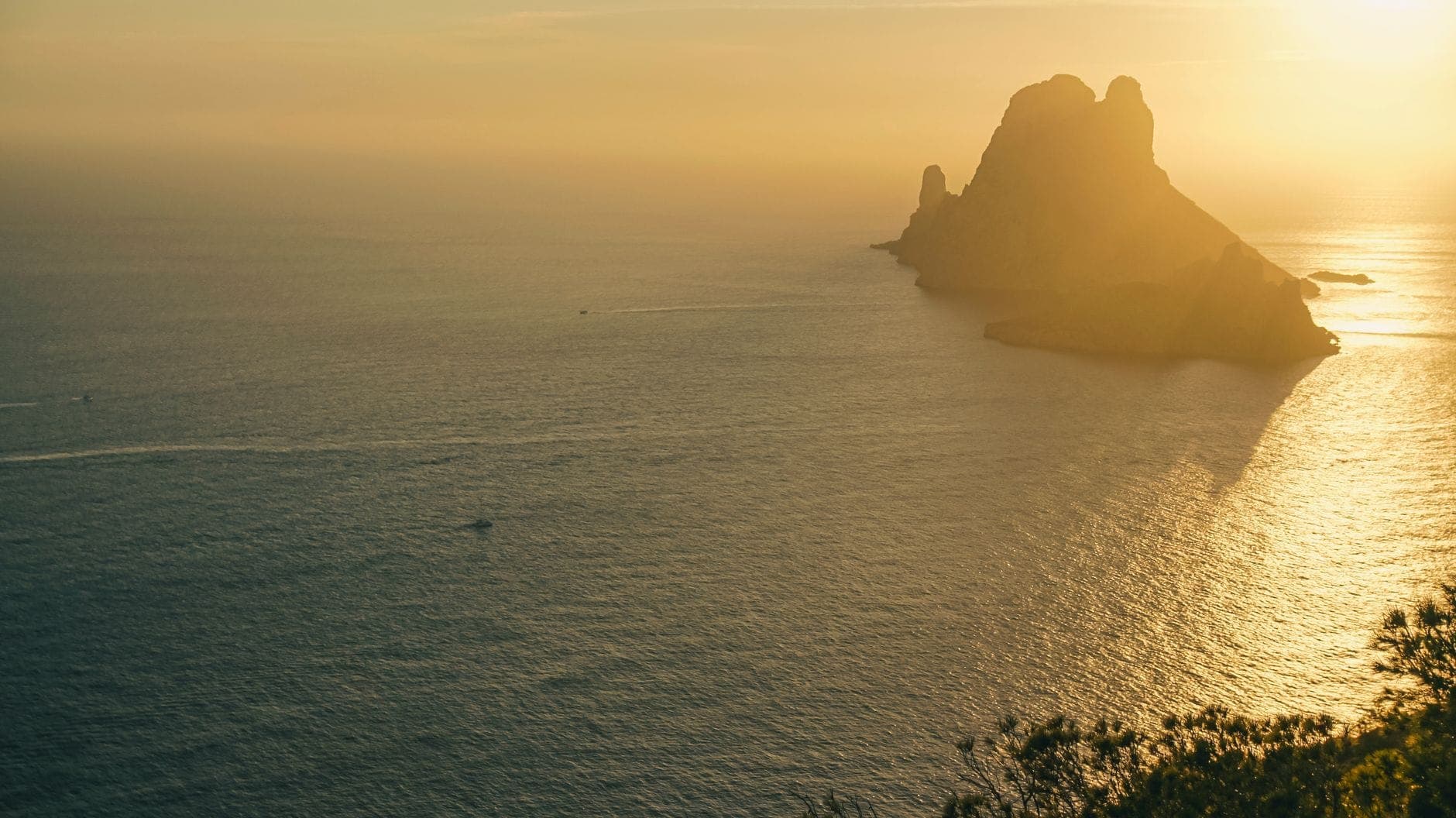 Golden sunset over the sea with the iconic Es Vedrà rock formation in silhouette, viewed from a high clifftop in Ibiza.