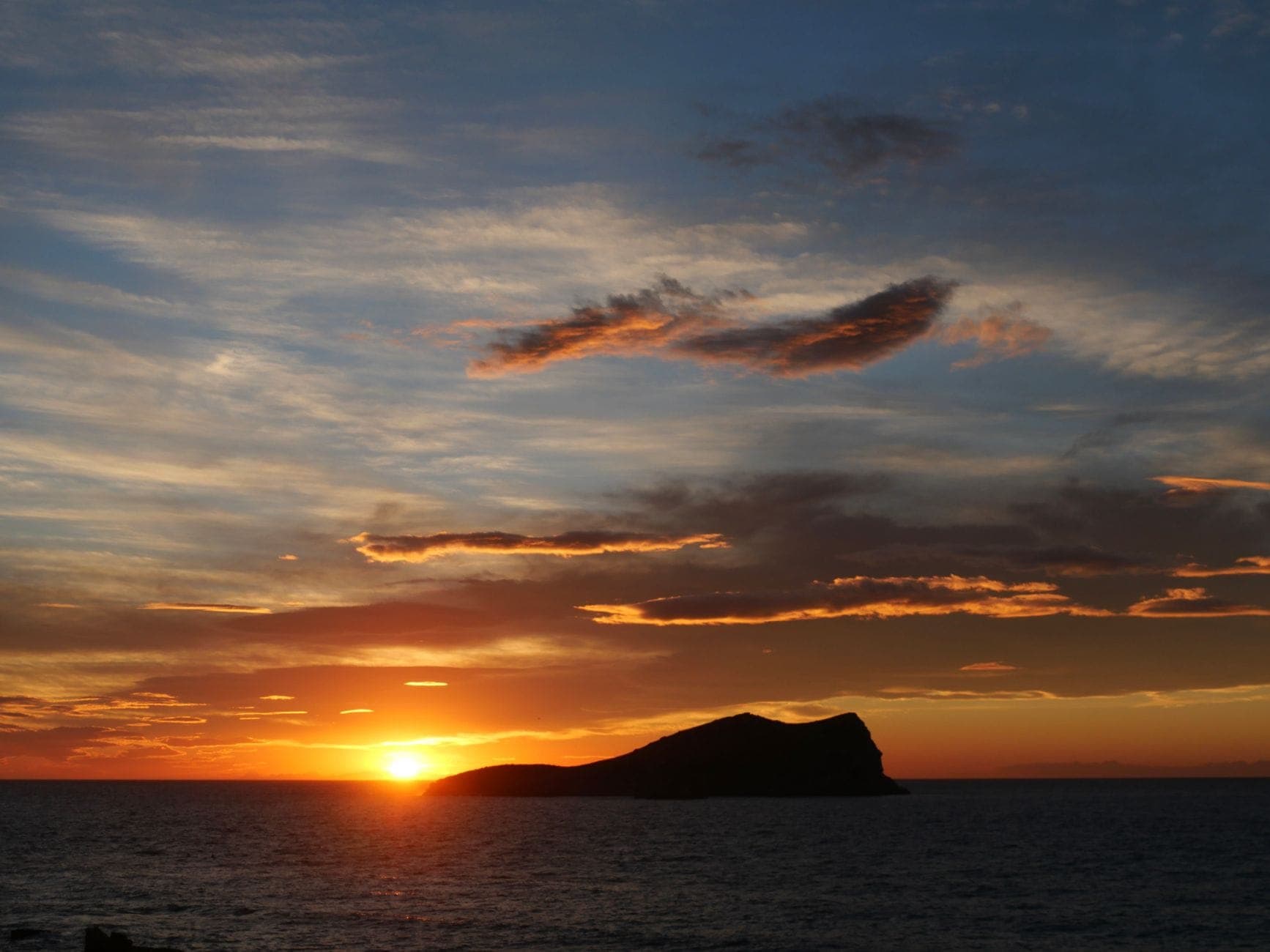 Golden sunset over the sea with a silhouetted island and colorful clouds, shot from the coastline in Ibiza.