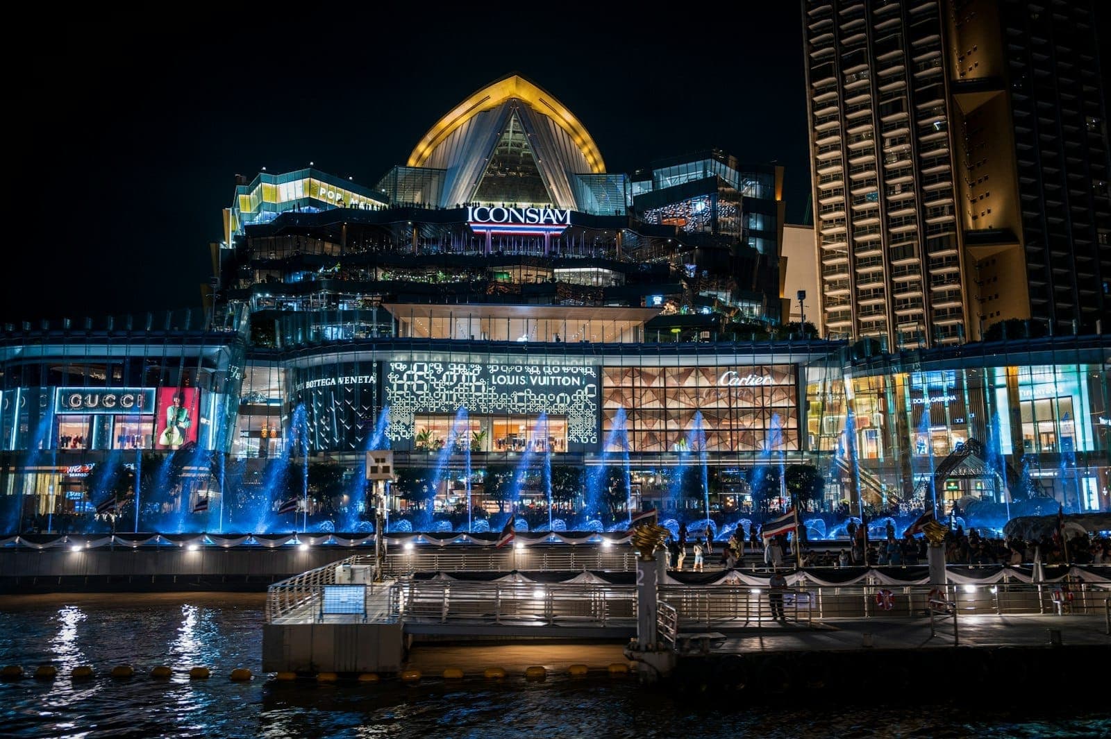 Trung tâm thương mại sang trọng IconSiam bên bờ sông Chao Phraya, Bangkok, với công viên ven sông, đài phun nước và các điểm thu hút văn hóa sôi động.