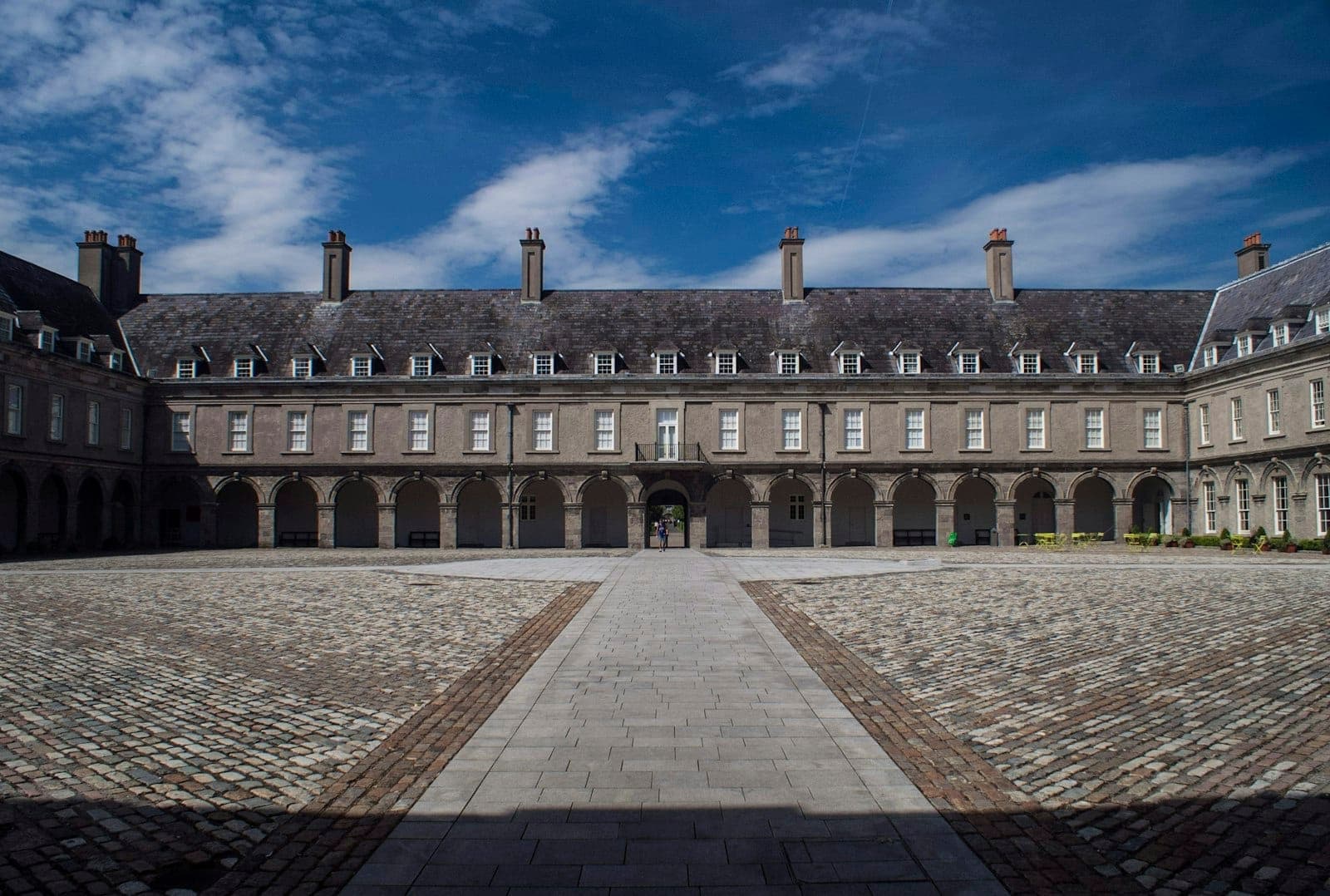 Weitwinkelaufnahme des gepflasterten Innenhofs des Royal Hospital Kilmainham mit historischer Fassade unter strahlend blauem Himmel – ein beeindruckender Blick auf die Architektur des IMMA aus dem 17. Jahrhundert.