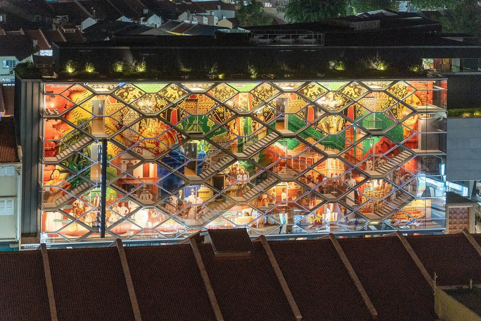 Nighttime view of the Indian Heritage Centre’s colorful, illuminated façade in Little India, featuring four floors with intricate patterns and cultural displays.