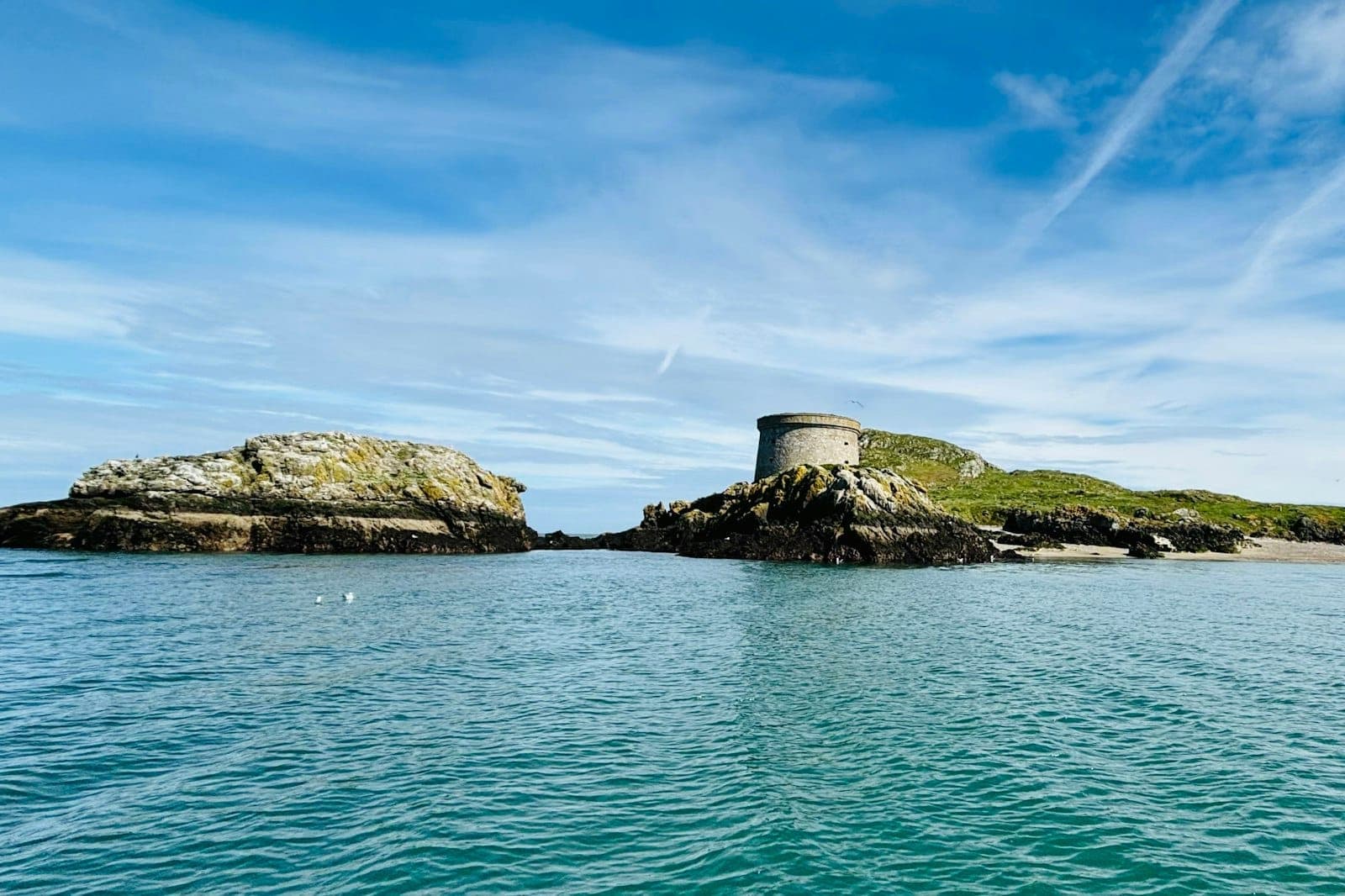Martello-Turm auf einem felsigen Vorsprung von Ireland's Eye, umgeben vom türkisfarbenen Meer und einem dramatischen Himmel – ein Blick auf die abgelegene, wilde Schönheit der Insel.