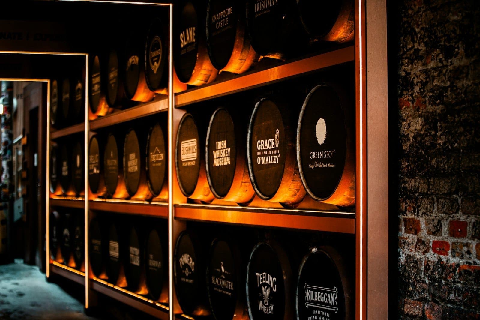 Ciepło oświetlona ściana beczek whiskey z nazwami różnych irlandzkich marek w muzeum lub destylarni w Dublinie.