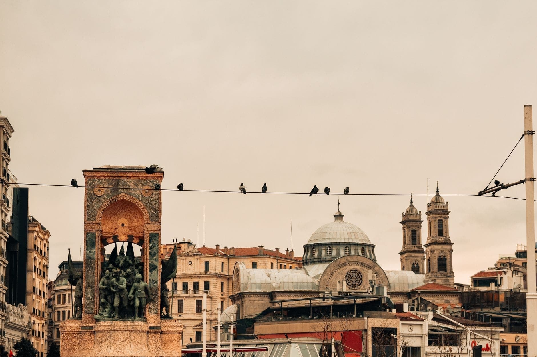 Lapangan Taksim dengan Monumen Republik, kabel trem di atas kepala, bangunan bersejarah, dan jalur trem yang terlihat di Istanbul.