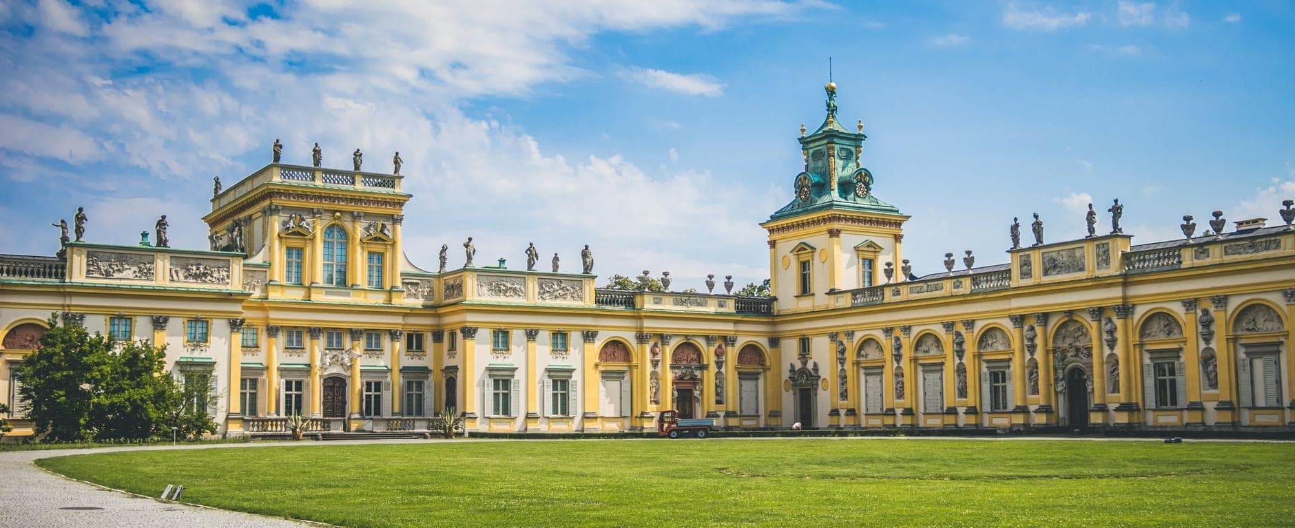 Weiter Blick auf das Wilanów-Palais in Warschau an einem sonnigen Tag mit blauem Himmel und grünem Rasen davor – beeindruckende Barockarchitektur.