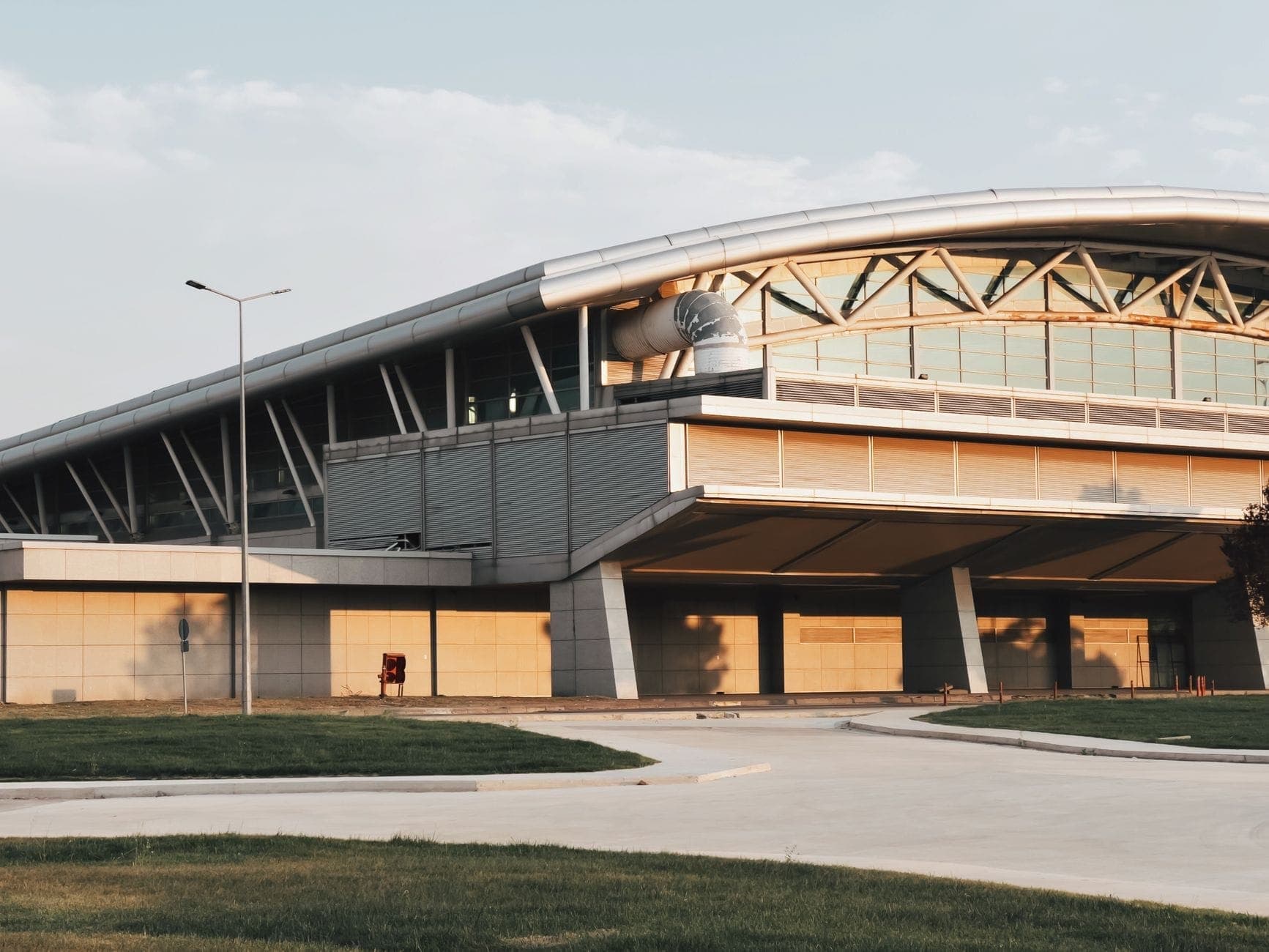 Esterno moderno del terminal dell'Aeroporto Sabiha Gökçen con tetto curvato, finestre in vetro e strada in primo piano in una giornata serena.