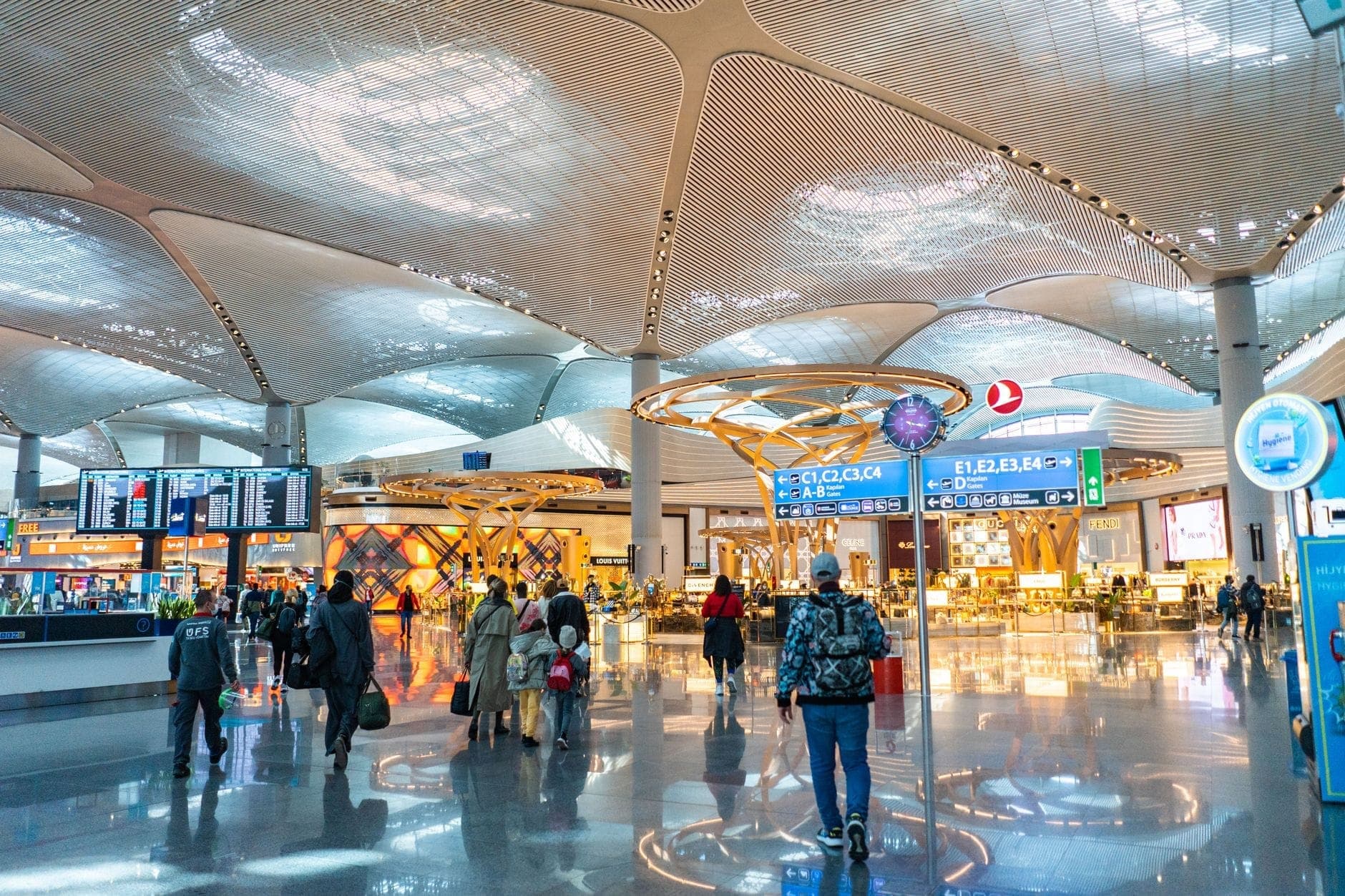 Interno spazioso e moderno del terminal dell'Istanbul Airport con passeggeri, segnaletica, sedute e dettagli architettonici del soffitto ben illuminati.