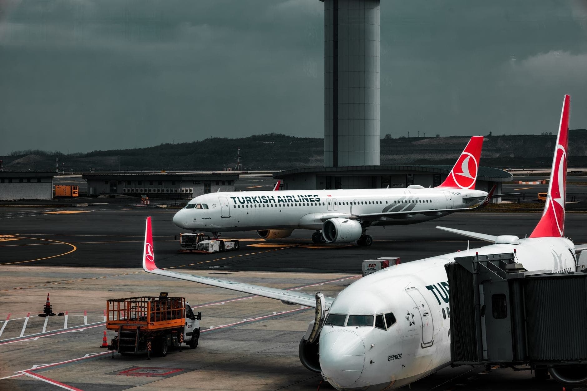 Turkish-Airlines-Maschinen am Gate und auf dem Rollfeld des Flughafens Istanbul, im Hintergrund das Terminal und der Kontrollturm unter dramatischem Himmel.