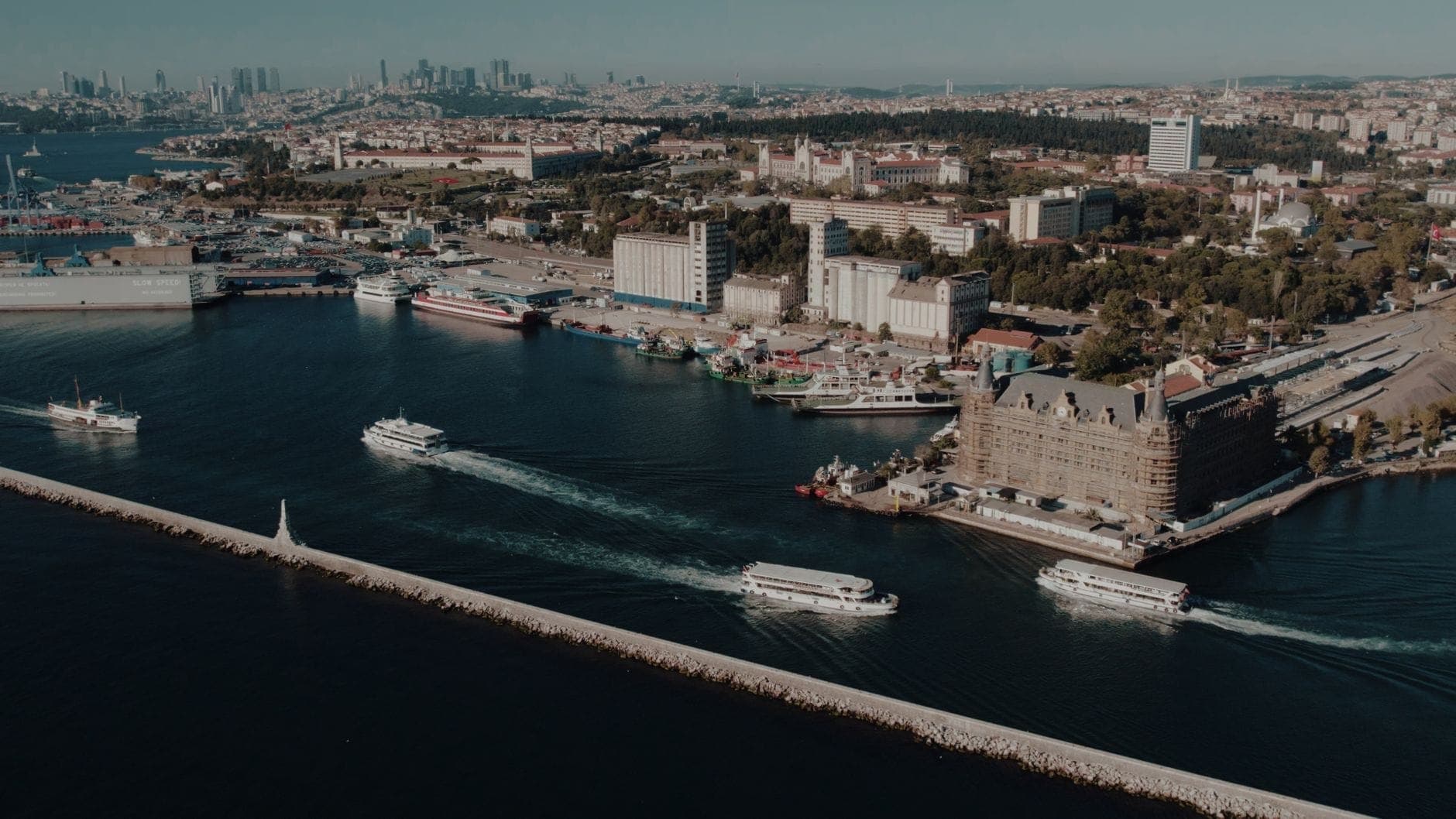 Luftaufnahme der Kadıköy-Uferpromenade mit Fähren auf dem Bosporus, dem historischen Bahnhof Haydarpaşa und der Skyline von Istanbuls asiatischer Seite im Hintergrund.