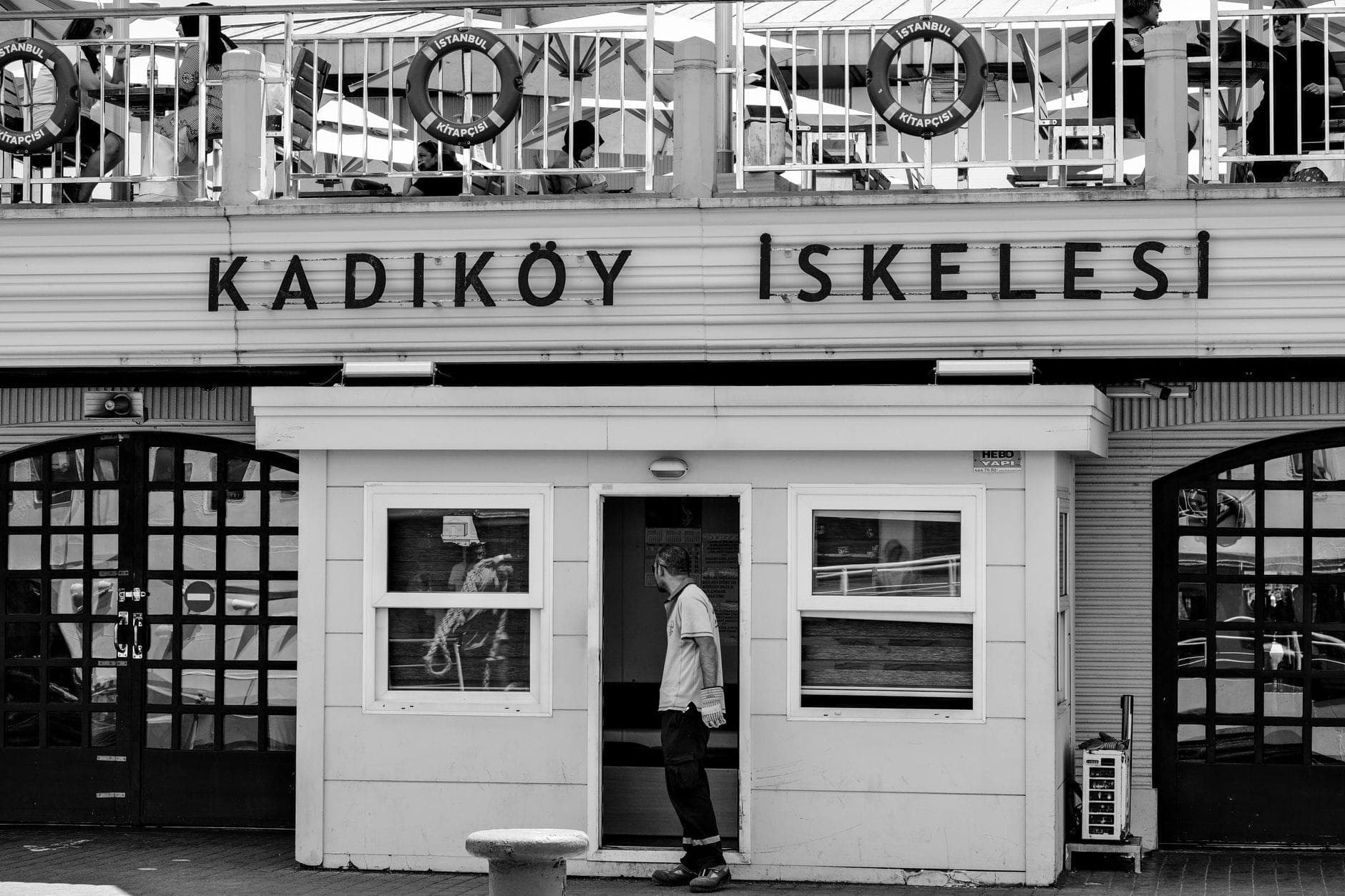 Schwarz-Weiß-Foto der Hauptfassade des Fährterminals Kadıköy, mit deutlicher Beschilderung und einer Person, die das Gebäude betritt.
