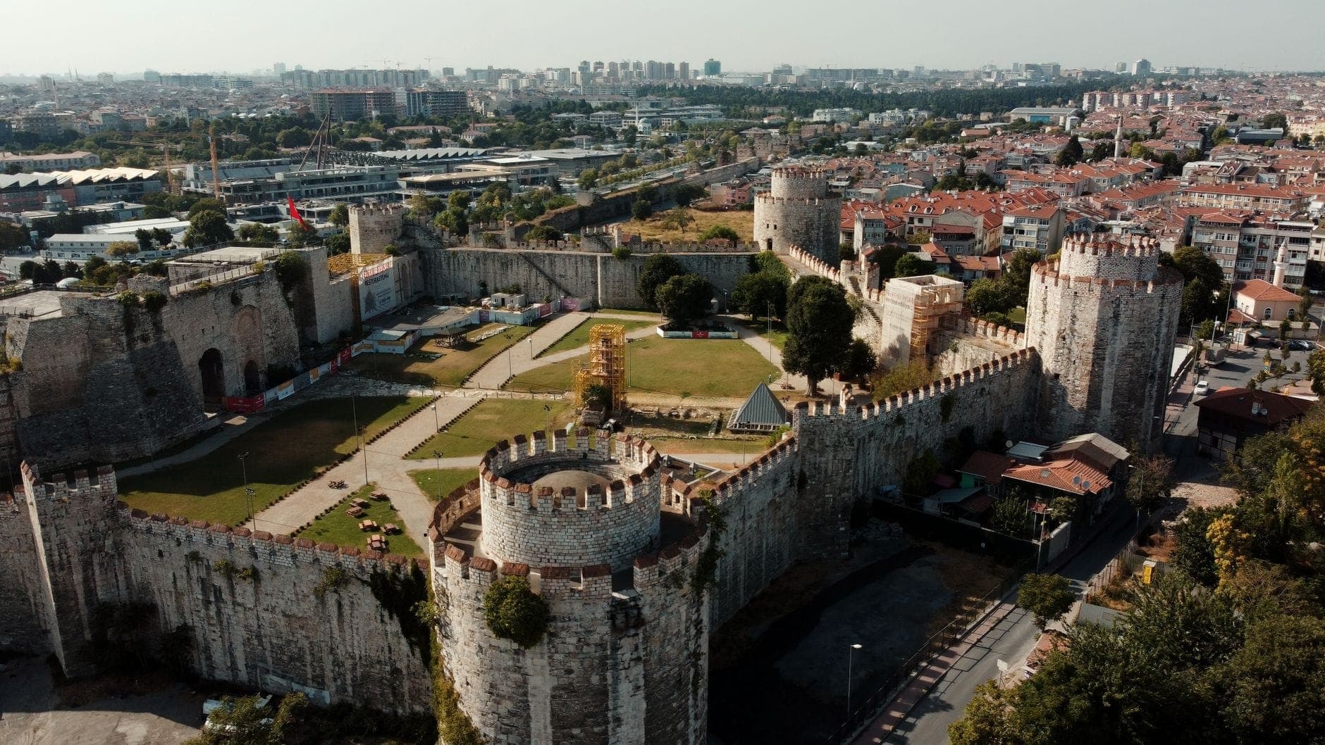 Widok z lotu ptaka na masywne Mury Teodozjańskie w Stambule, ukazujący solidne kamienne wieże, blanki i panoramę miasta w tle.