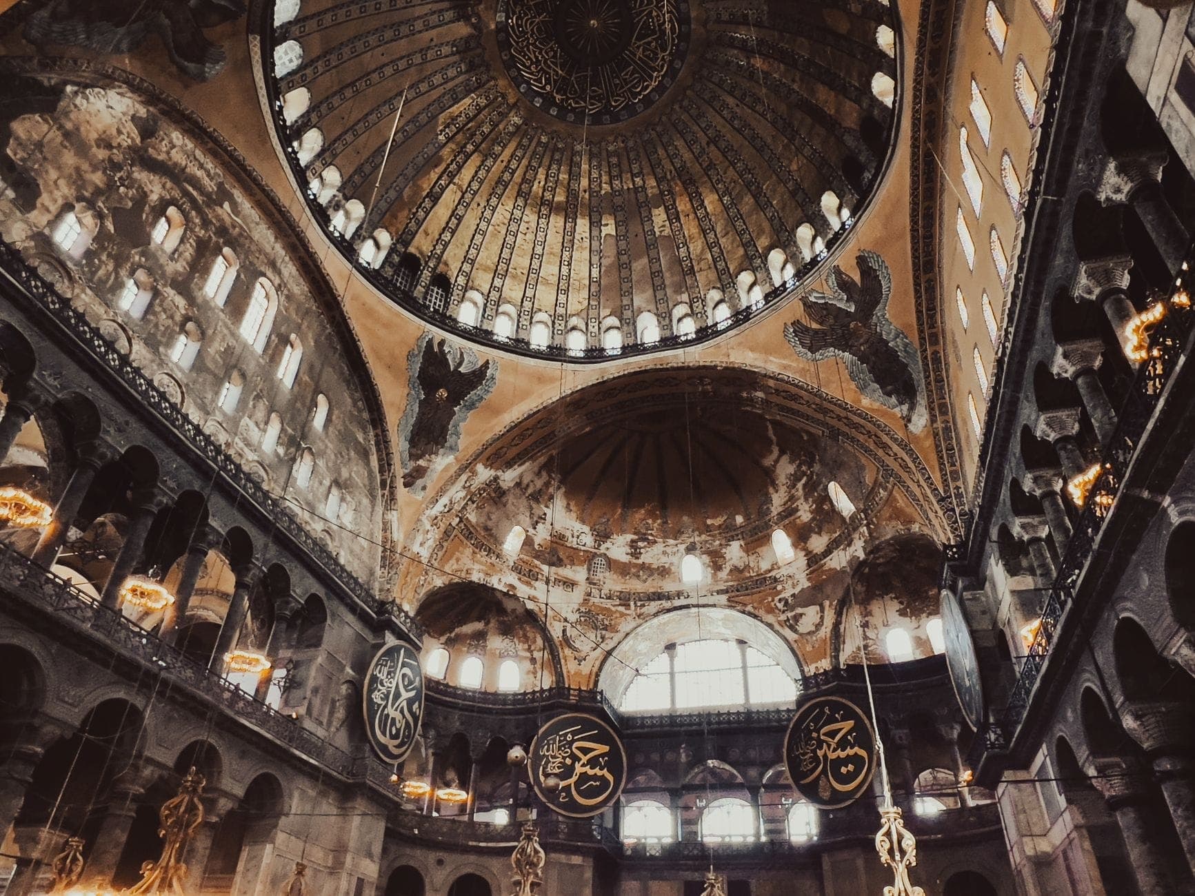 Szeroki widok wnętrza Hagia Sophia ukazujący wspaniałe kopuły, mozaiki bizantyjskie, islamską kaligrafię i okna łukowe z wpadającym naturalnym światłem.