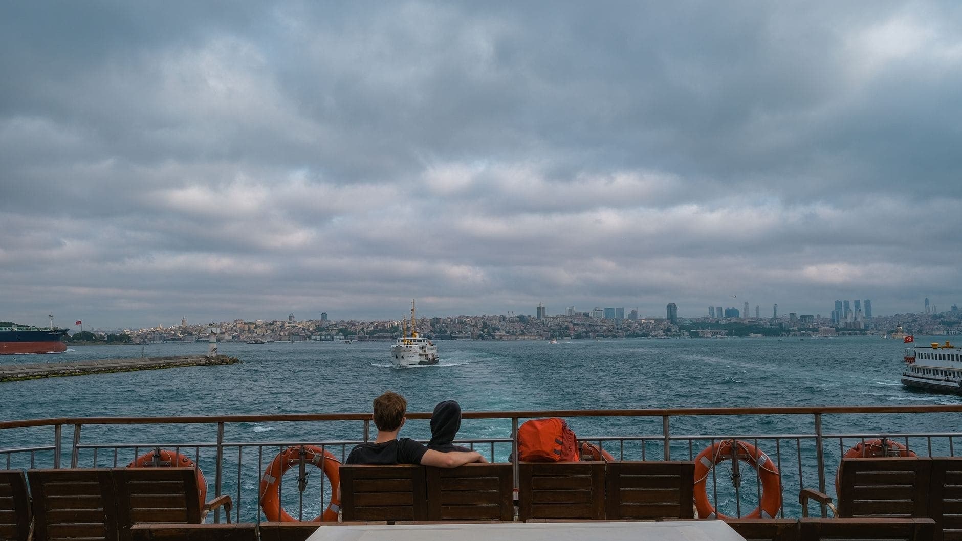 Paar, das eng beieinander auf einer Fähre sitzt, mit Blick auf die Ufersilhouette von Istanbul und anderen Fähren auf dem Bosporus.