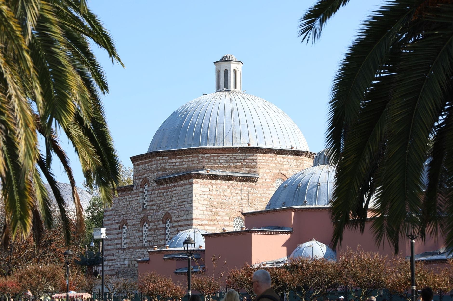 Historisches Kuppelgebäude eines türkischen Hamams in Istanbul, umgeben von Palmen und klarem Himmel.