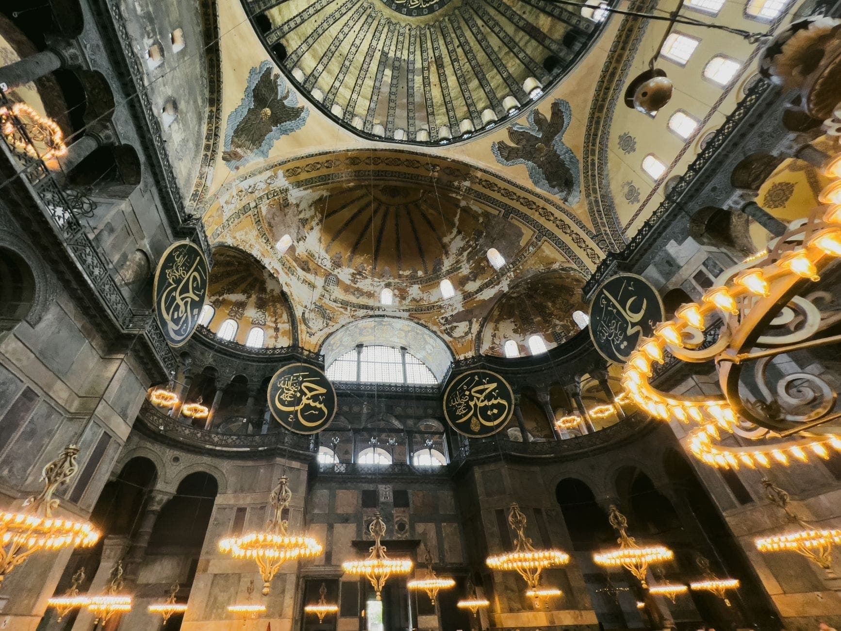 Vista interior de Hagia Sophia con elaboradas cúpulas, arañas de luces, grandes arcos y enormes medallones caligráficos en Estambul.