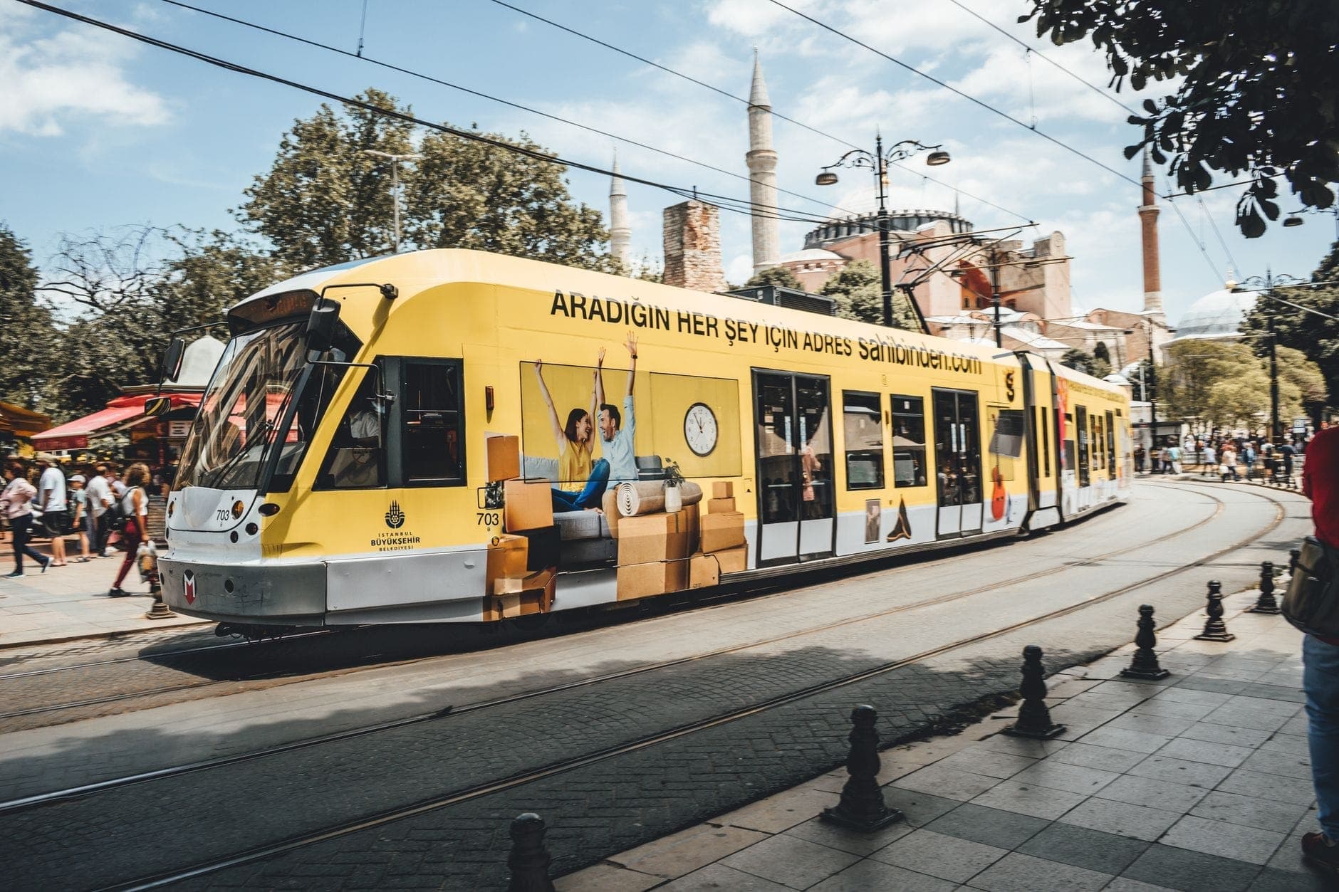 Tranvía moderno pasando por una calle concurrida con la Hagia Sophia al fondo en la península histórica de Estambul.