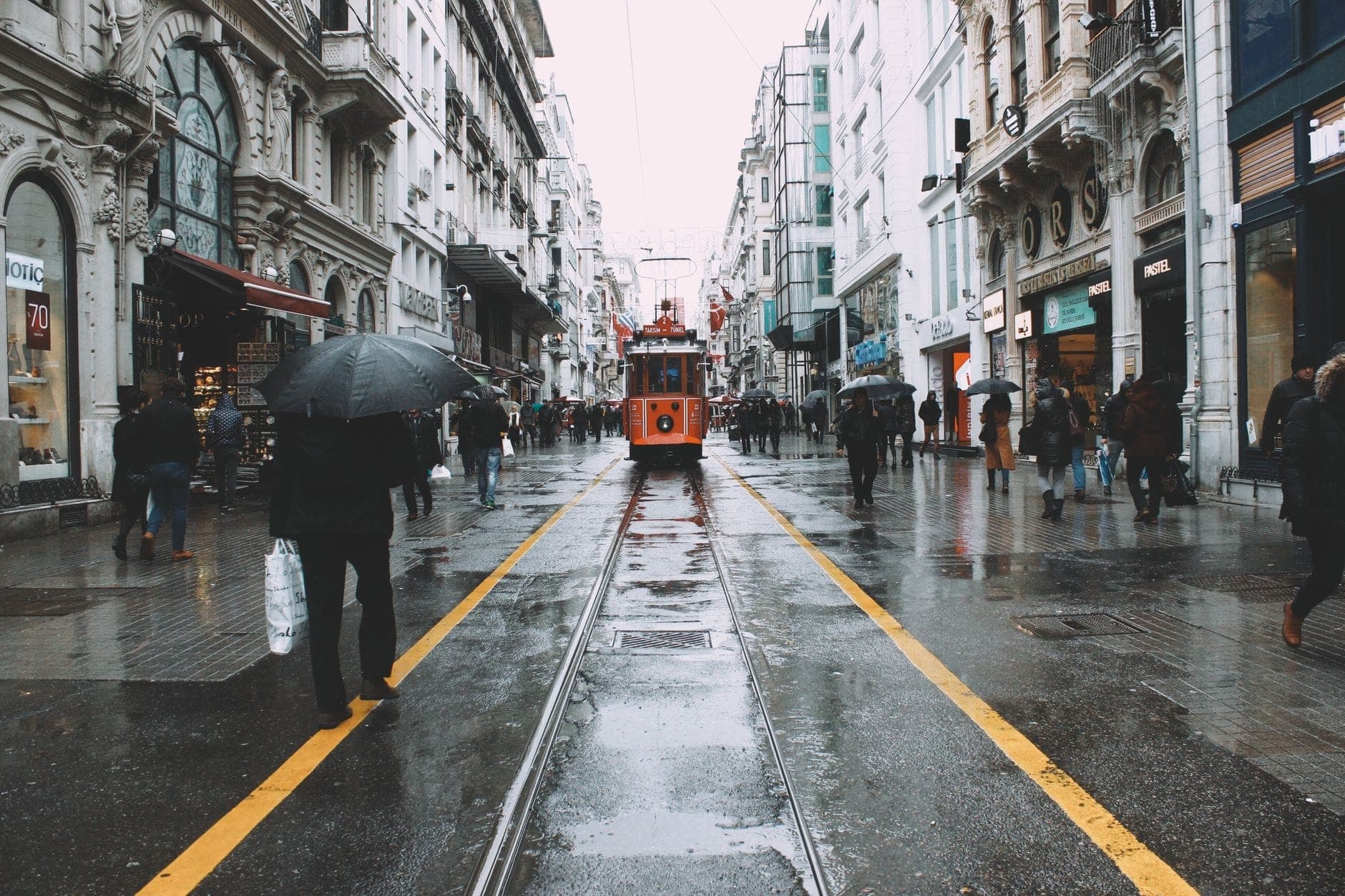 People walking with umbrellas on a wet Istiklal Avenue in Istanbul, with the iconic red tram at the center of the rainy street.