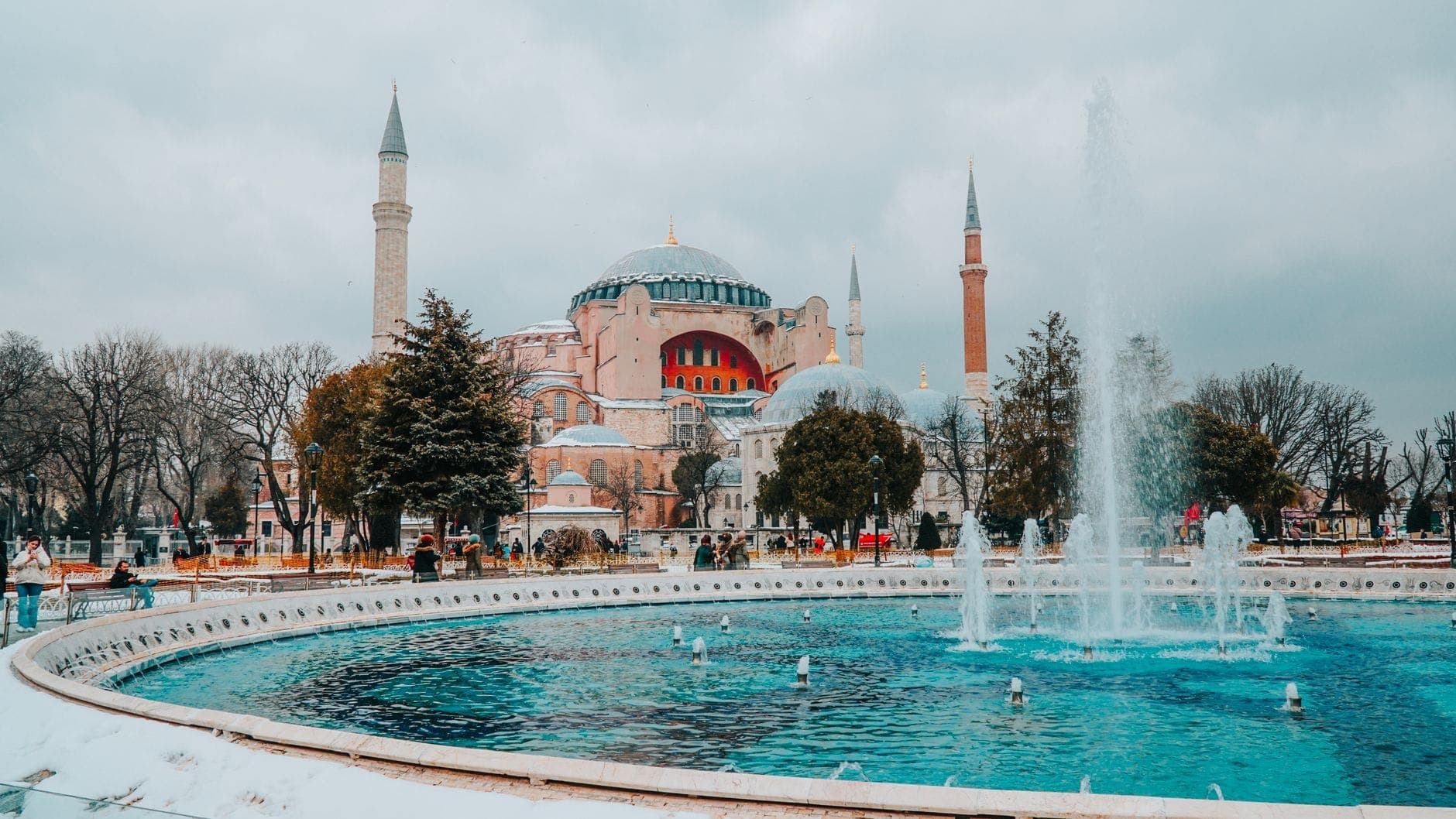 Hagia Sophia zimą ze śniegiem na ziemi, dużą fontanną na pierwszym planie i zachmurzonym niebem nad Stambułem.