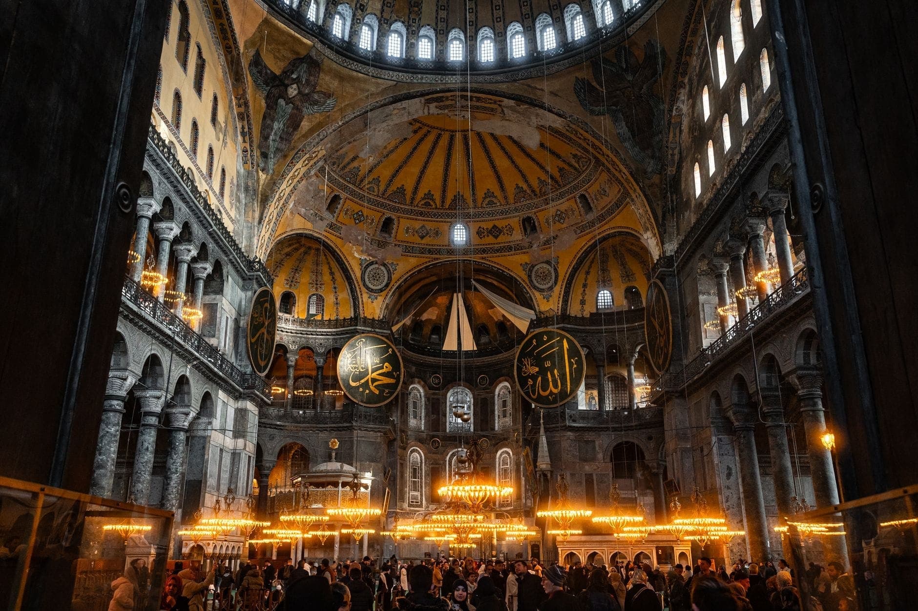 Szeroki widok wnętrza Hagia Sophia w Stambule z tłumami odwiedzających, ozdobnymi żyrandolami i wspaniałą architekturą kopułową, idealny do zwiedzania zimą.